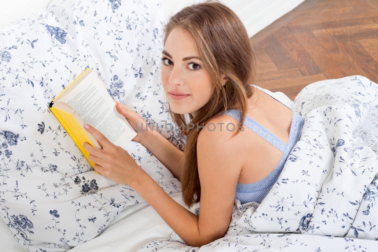 young attractive woman reading book lying in bed at home