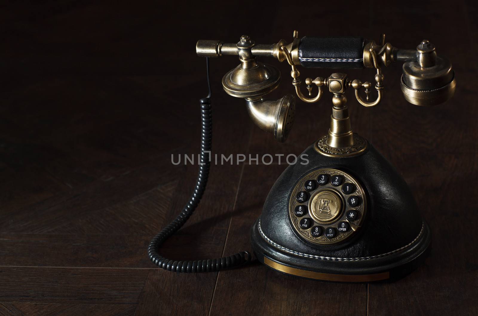 Old vintage or antique rotary phone with a handset and cradle on a dark shadowed background with copyspace
