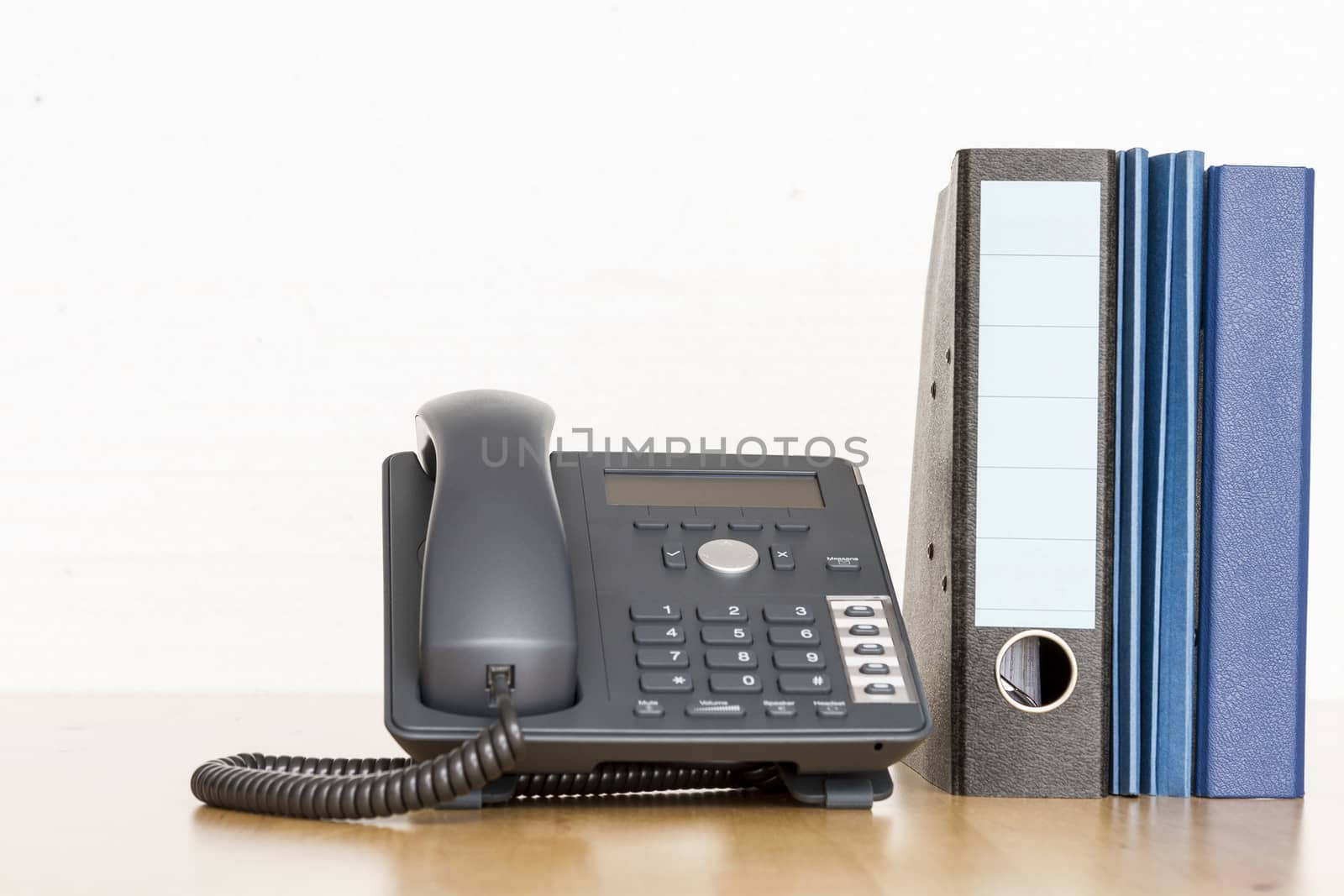 modern business phone with ring binder an folder on wooden desk