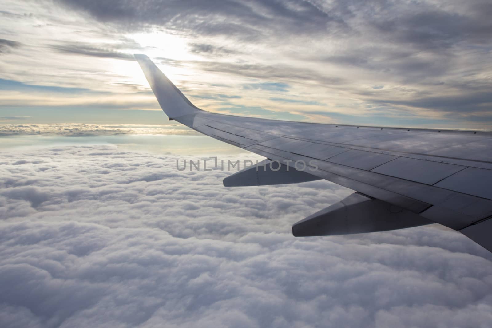 Sunset, cloudy sky and airplane wing as seen through window of an aircraft.