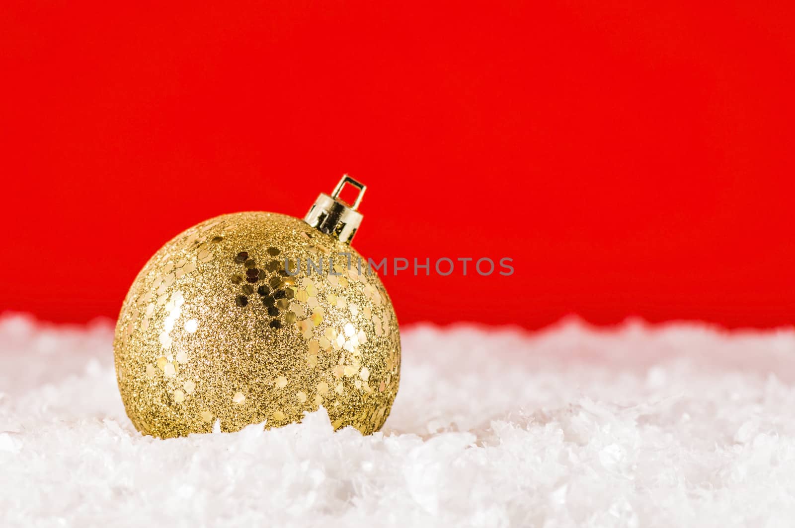 Golden Christmas decoration in artificial snow on red backgtound