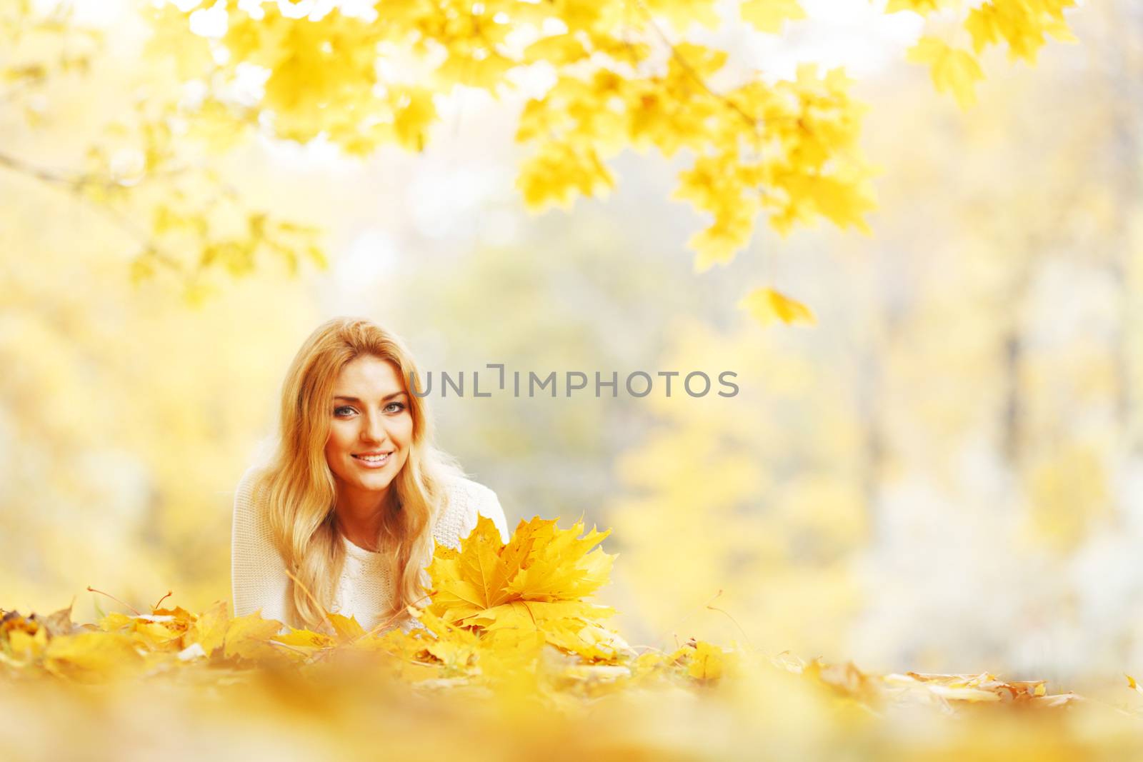 Young woman laying down on the ground covered dry autumnal foliage in beautiful park