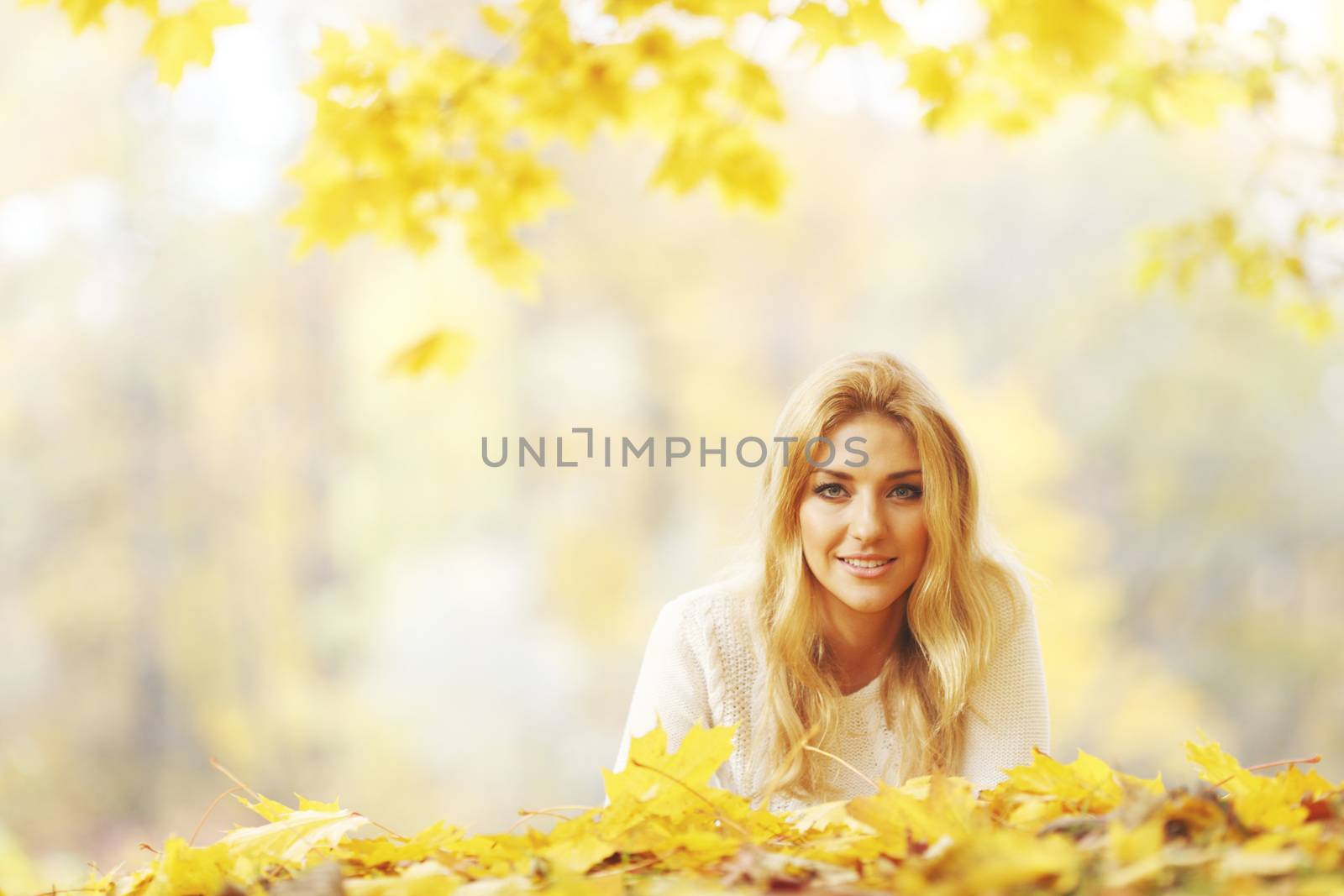 Young woman laying down on the ground covered dry autumnal foliage in beautiful park