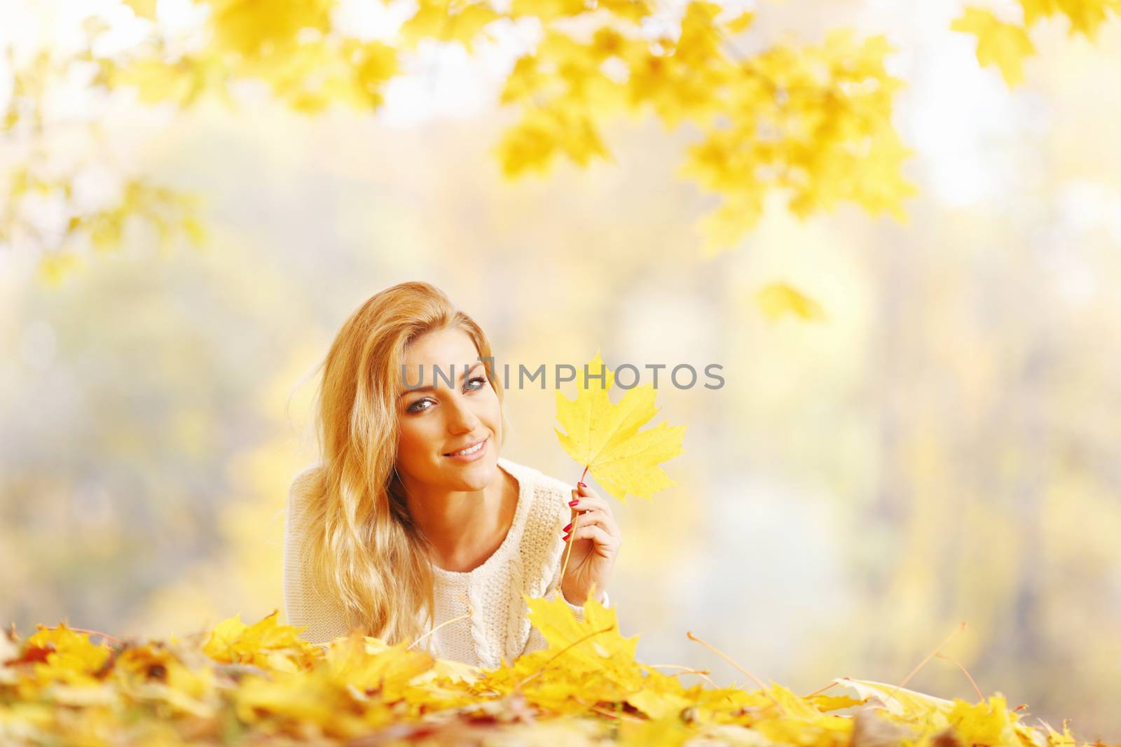 Young woman laying down on the ground covered dry autumnal foliage in beautiful park