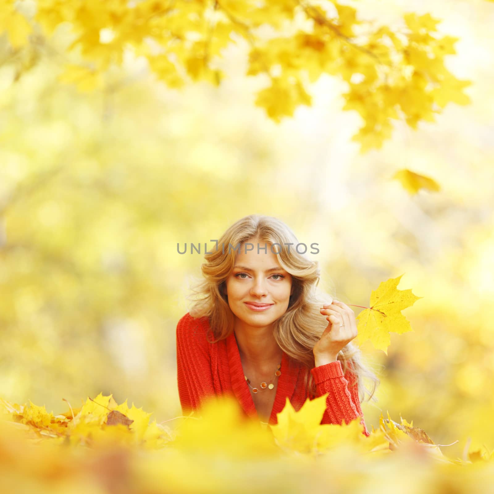 Happy young woman laying on autumn leaves in park