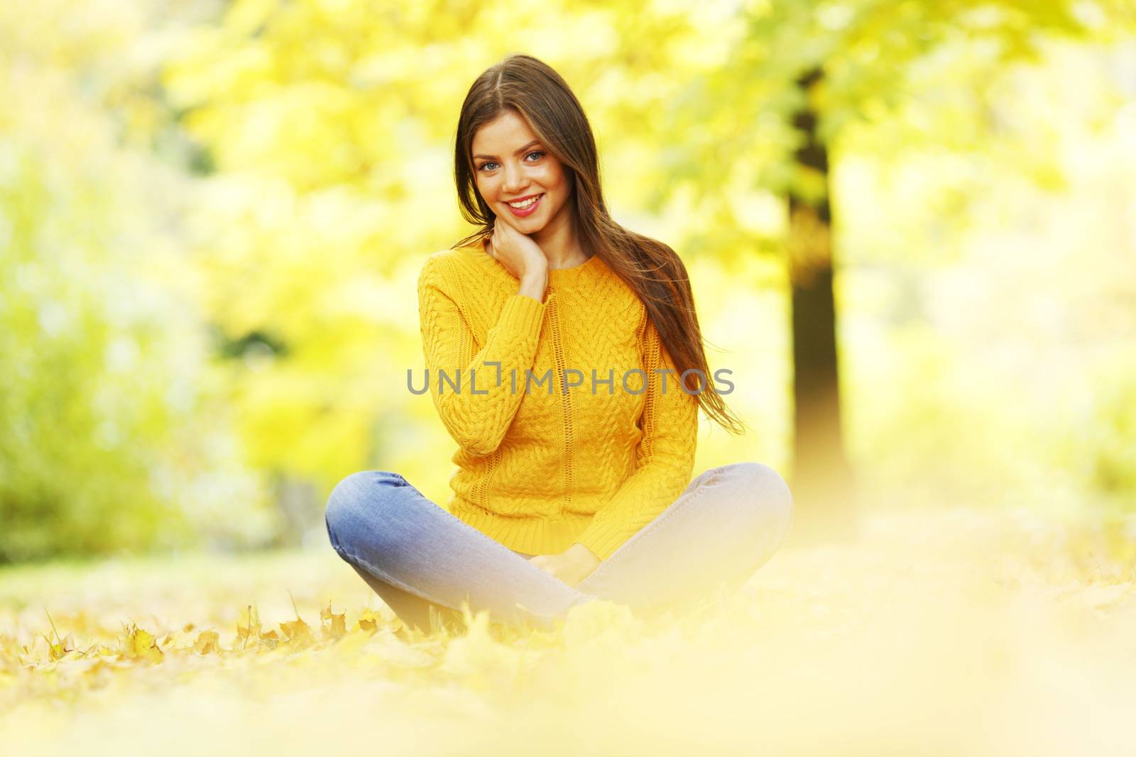 Beautiful woman sitting on autumn leaves in park