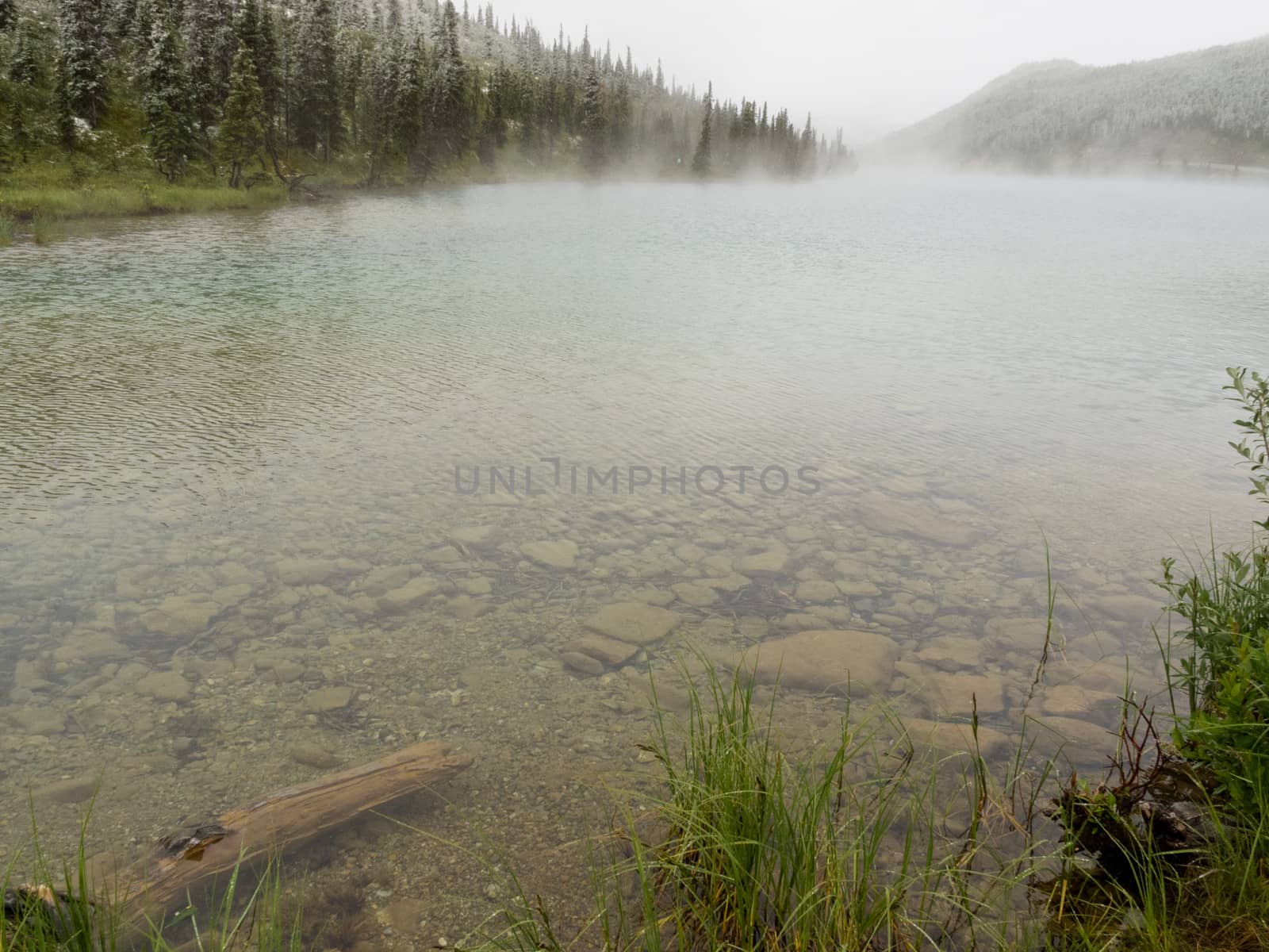 Clear water of boreal forest taiga mountain lake steaming after cold bad weather snow fell in summer