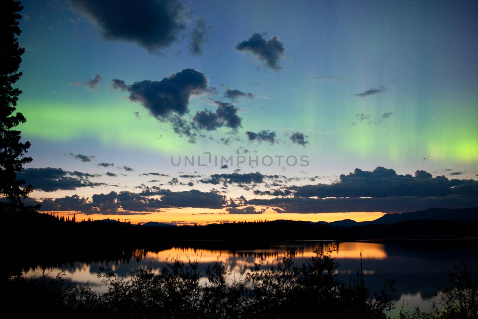 Northern lights Aurora borealis at midnight in summer over northern horizon of Lake Laberge Yukon Territory Canada midnight sun just below