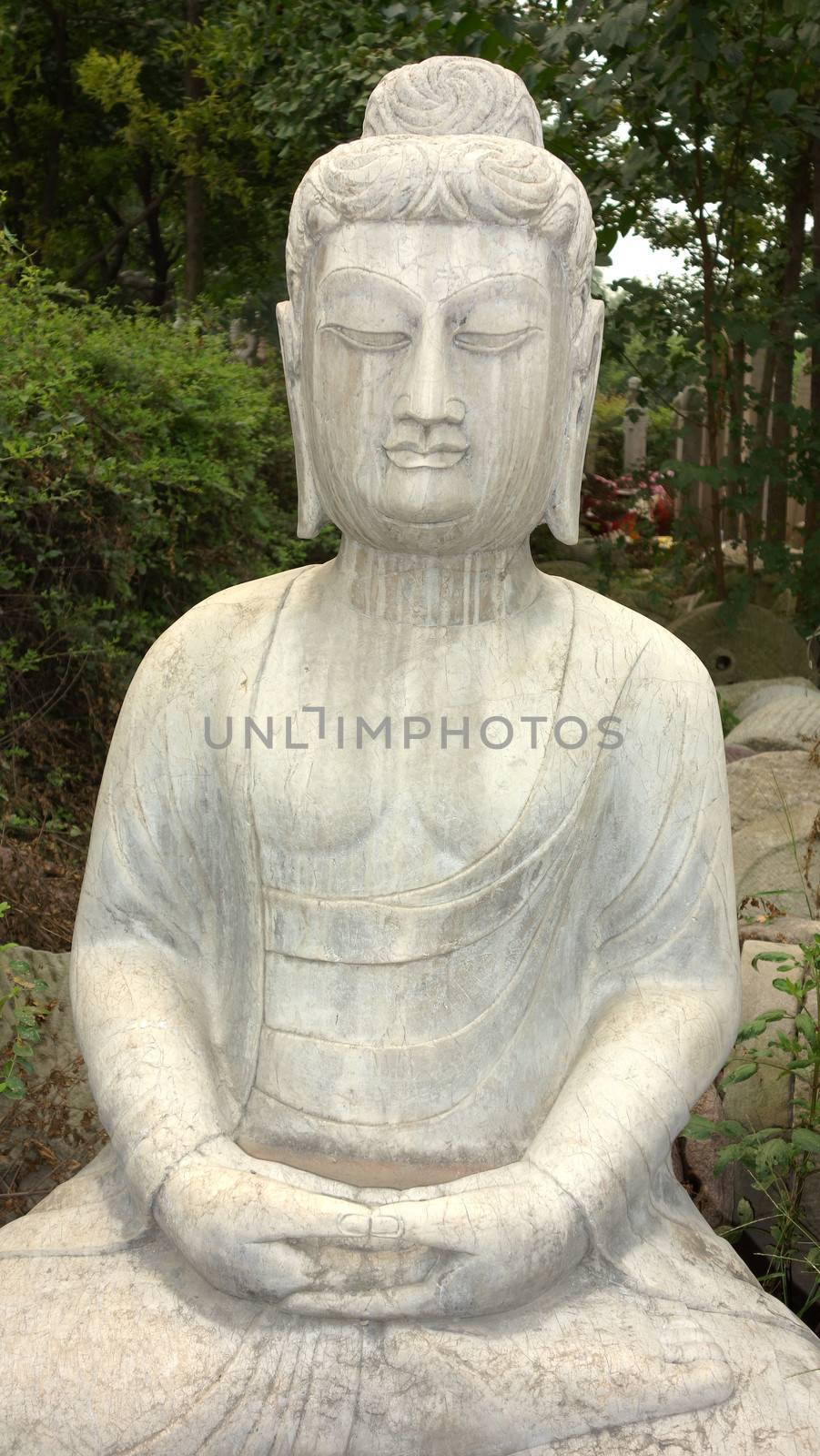 Ancient Buddha stone statue against green woods 