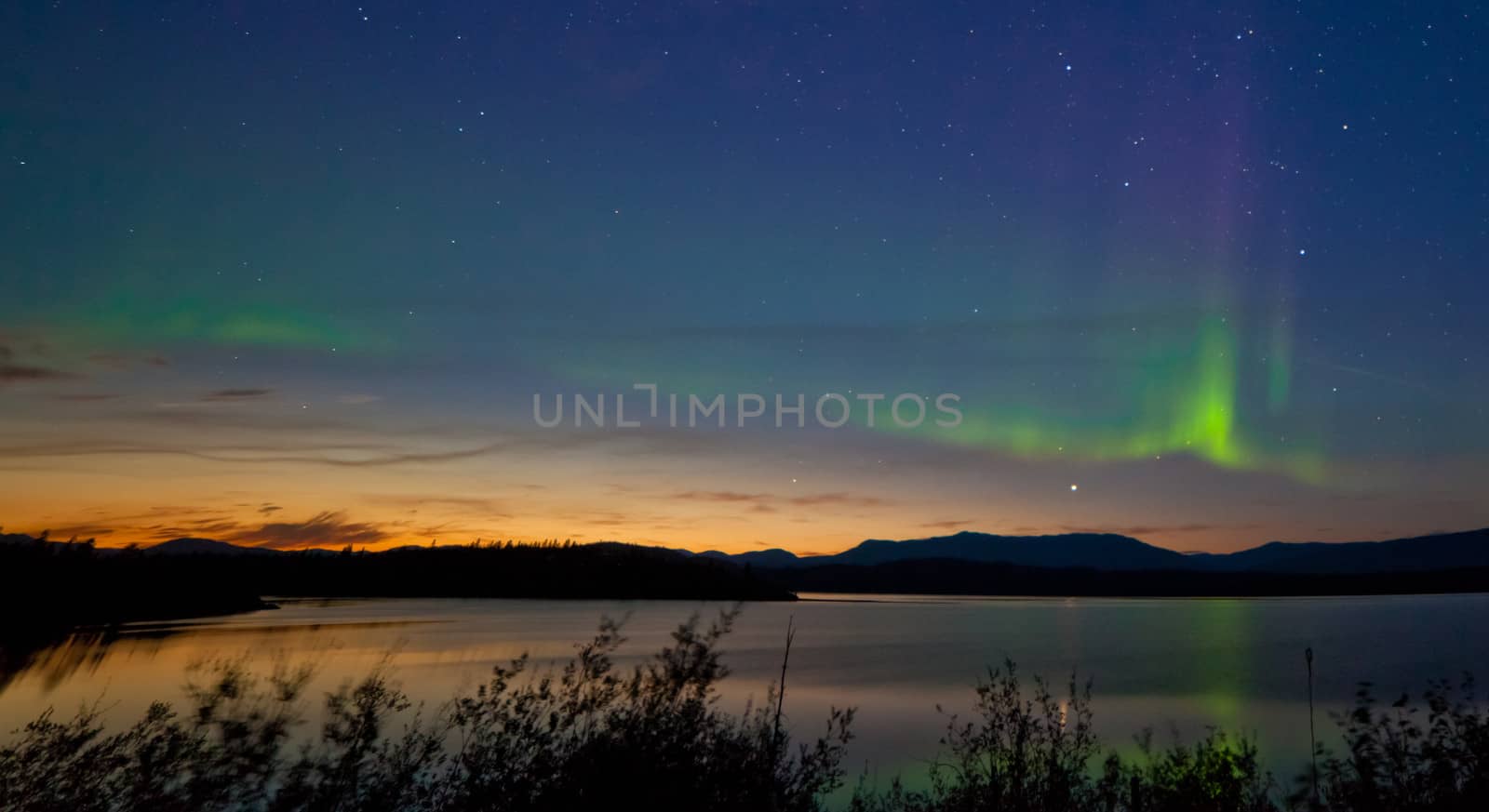 Northern lights Aurora borealis at midnight in summer over northern horizon of Lake Laberge Yukon Territory Canada at early dawn