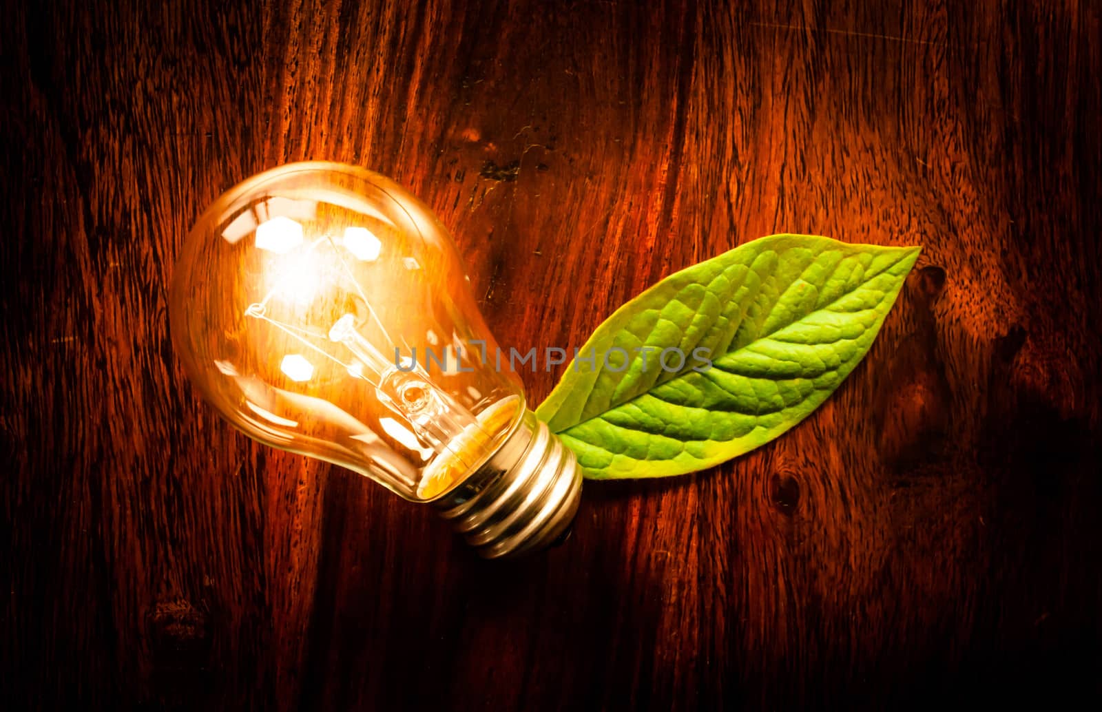 Bright light bulb with a green leaf at a wooden table