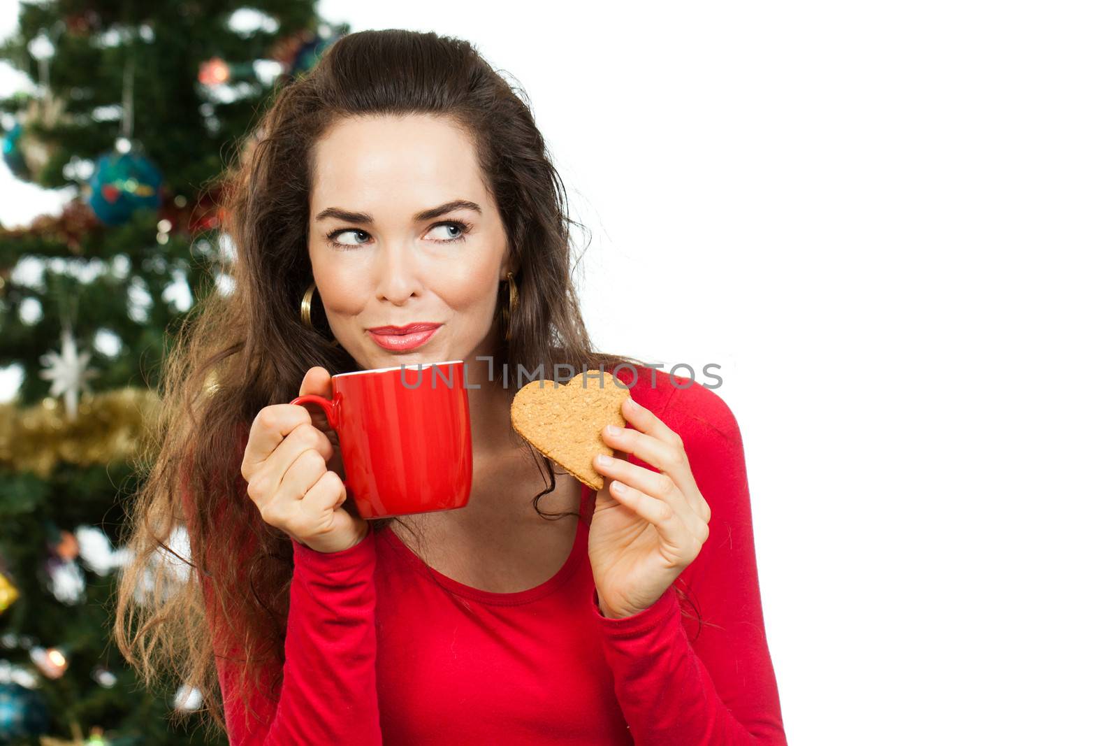 Beautiful woman enjoying a hot drink and gingerbread cookie in front of a Christmas tree. Isolated on white.
