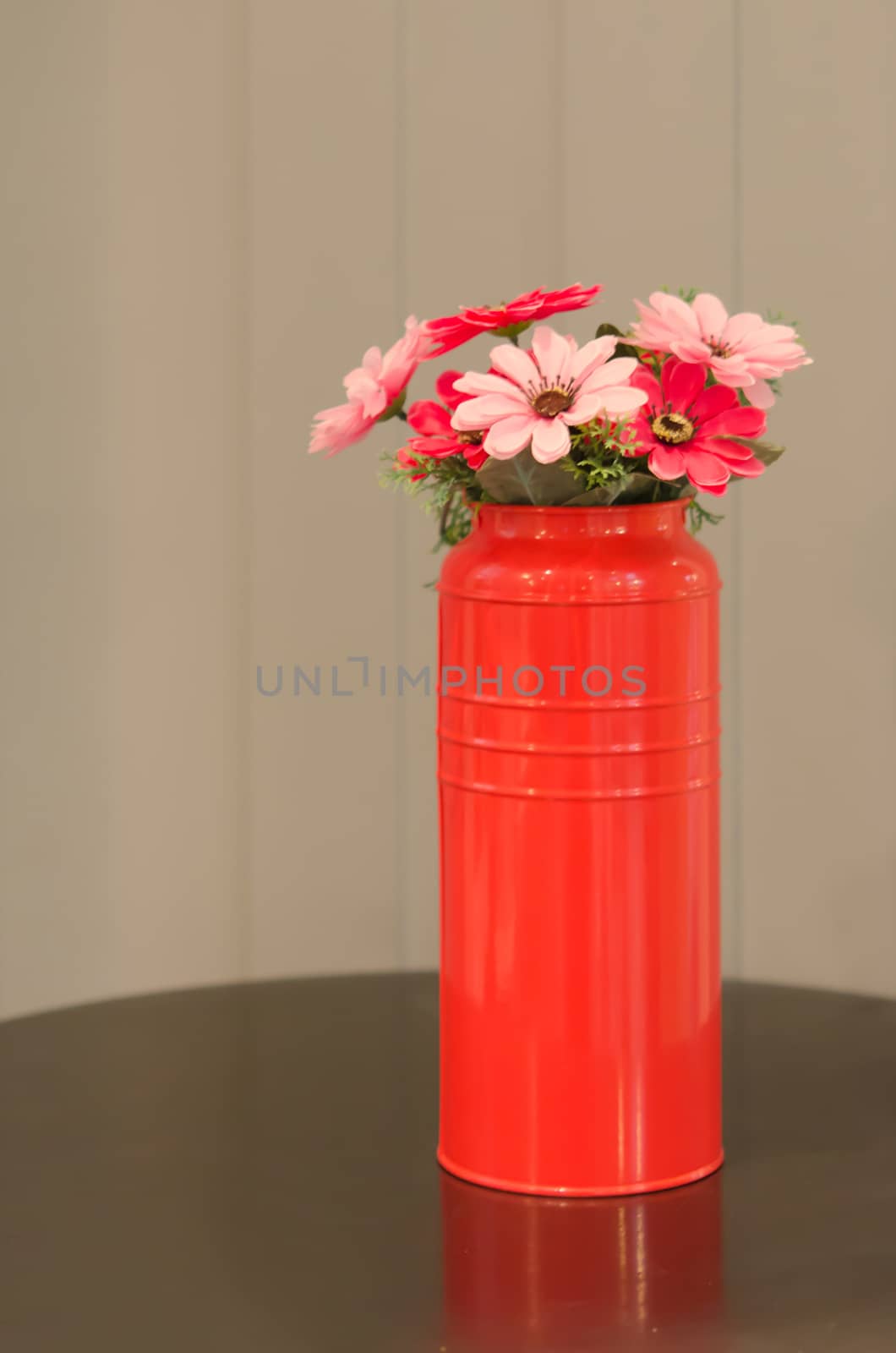 plastic  flowers with leaves  in red vase on  table , 