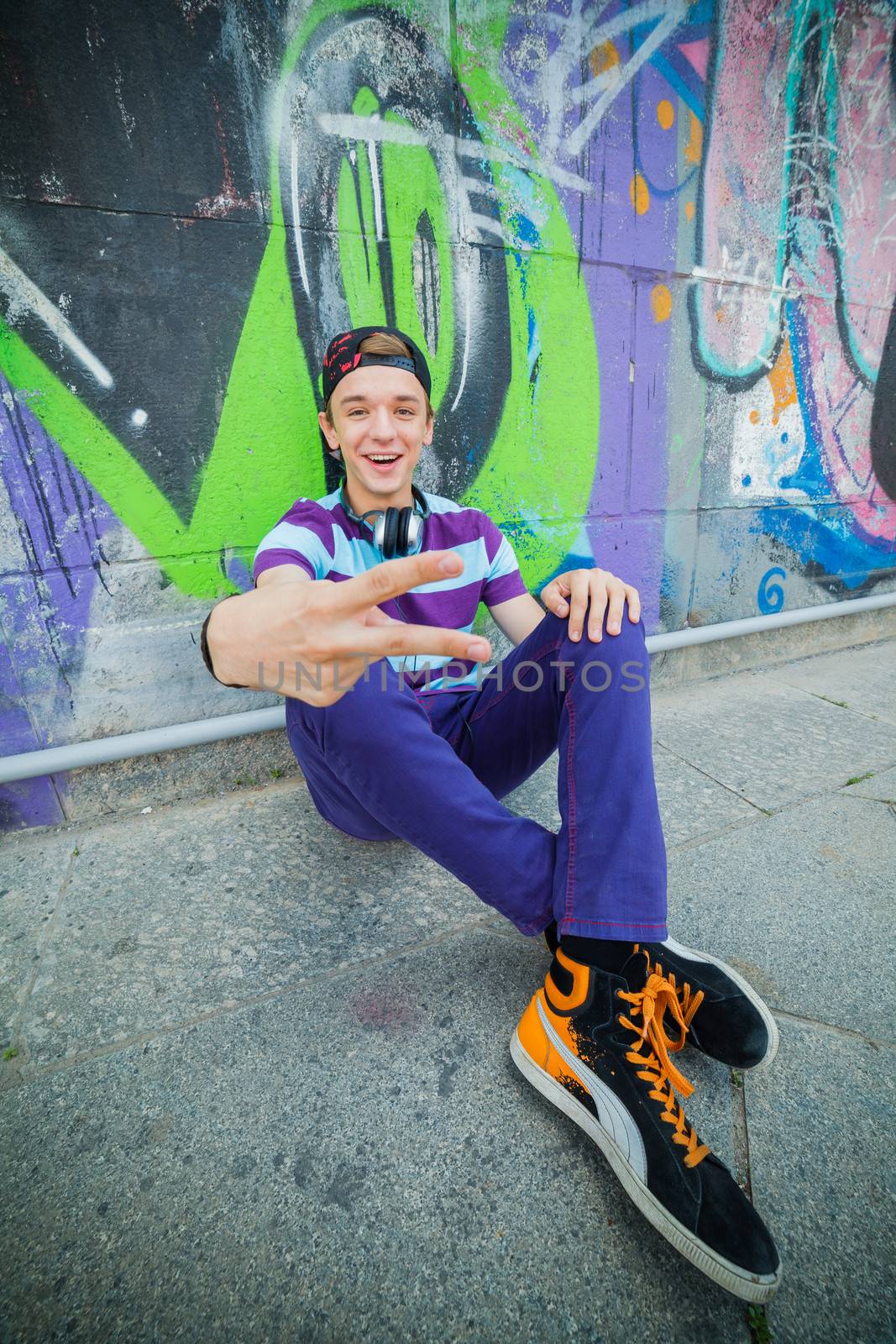 Happy teens boy with headphones near painted wall listening to music