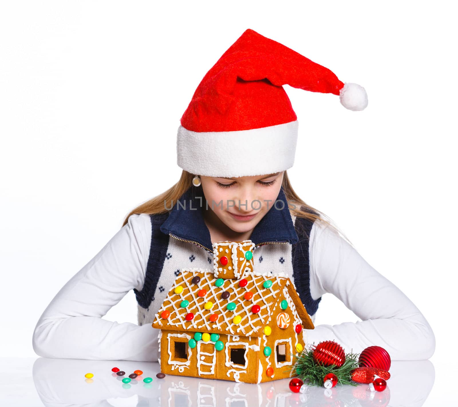 Christmas theme - Smiling girl in Santa's hat with gingerbread house, isolated on white