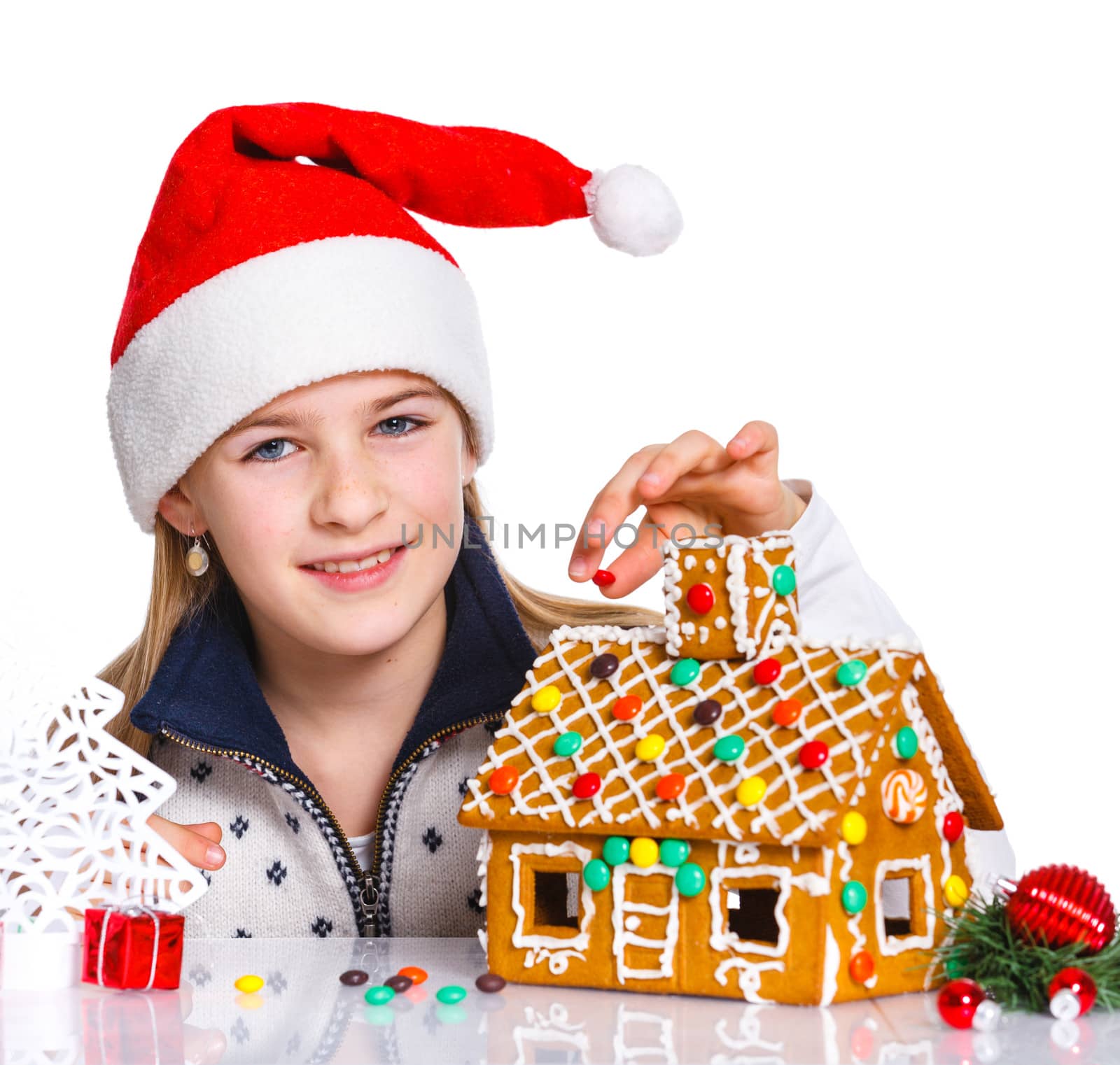 Christmas theme - Smiling girl in Santa's hat with gingerbread house, isolated on white