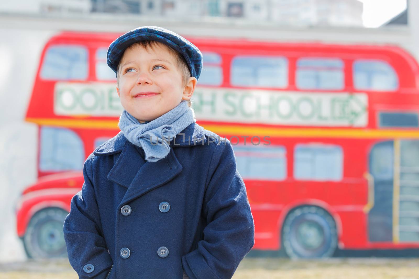 Little detective. Funny boy looking up and standing near english schoolbus