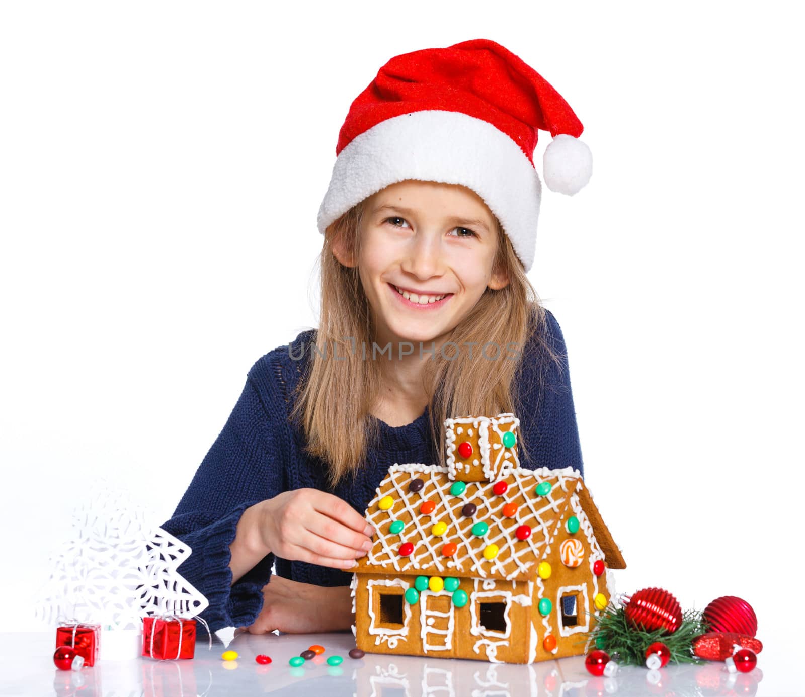 Christmas theme - Smiling girl in Santa's hat with gingerbread house, isolated on white