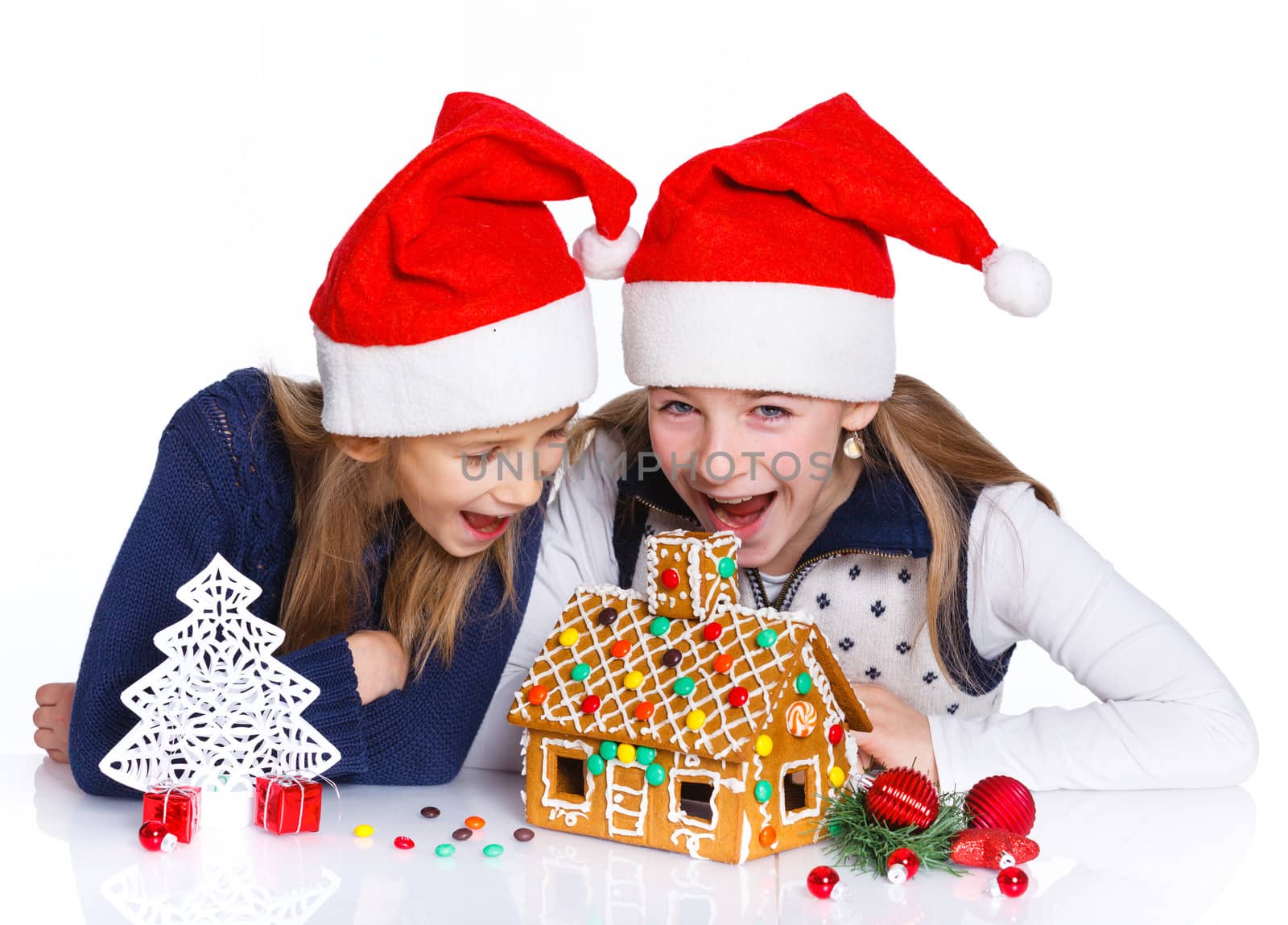 Christmas theme - Two smiling girl in Santa's hat with gingerbread house, isolated on white