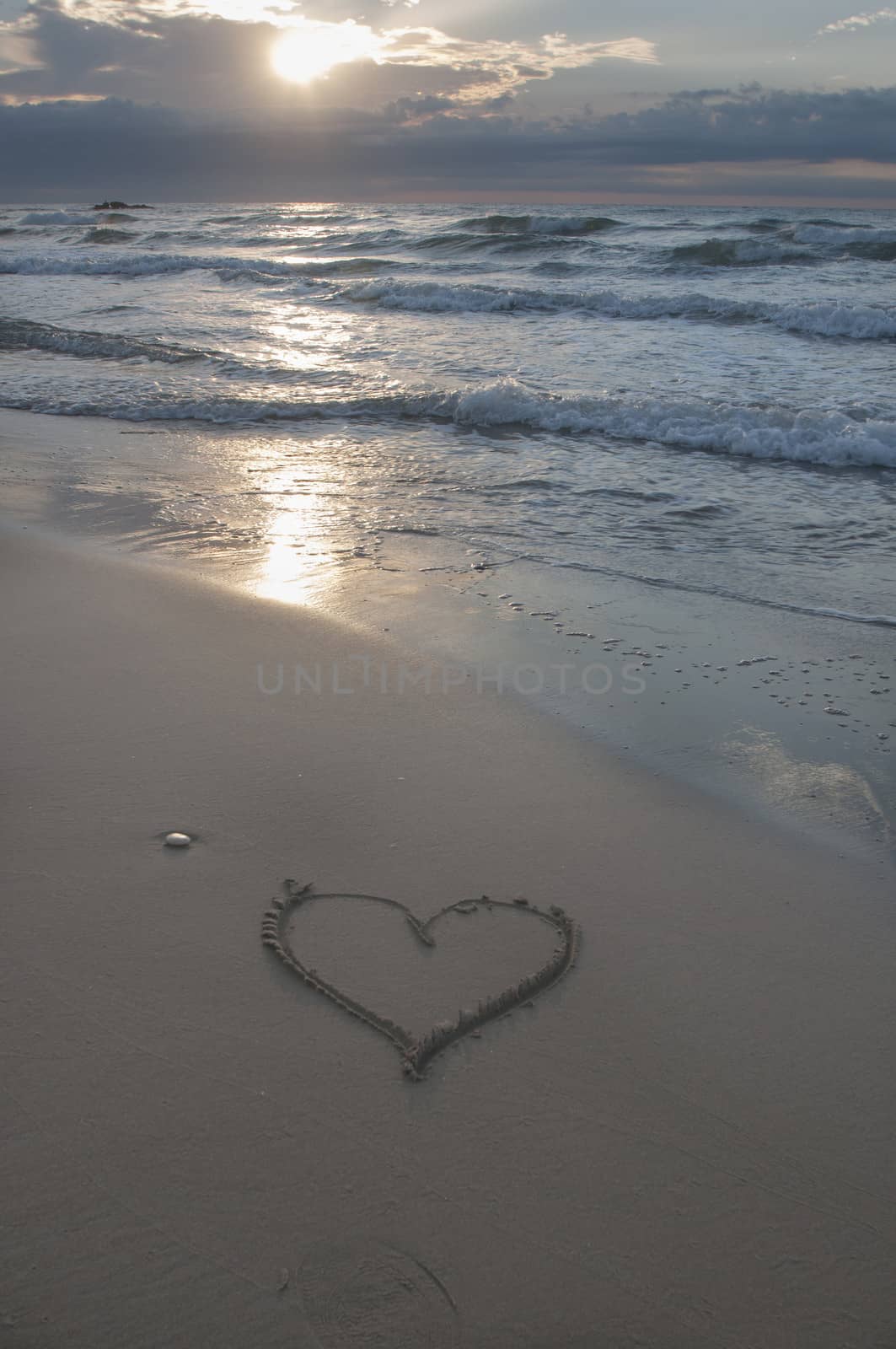 Sunset on the beach with heart drawn in the sand