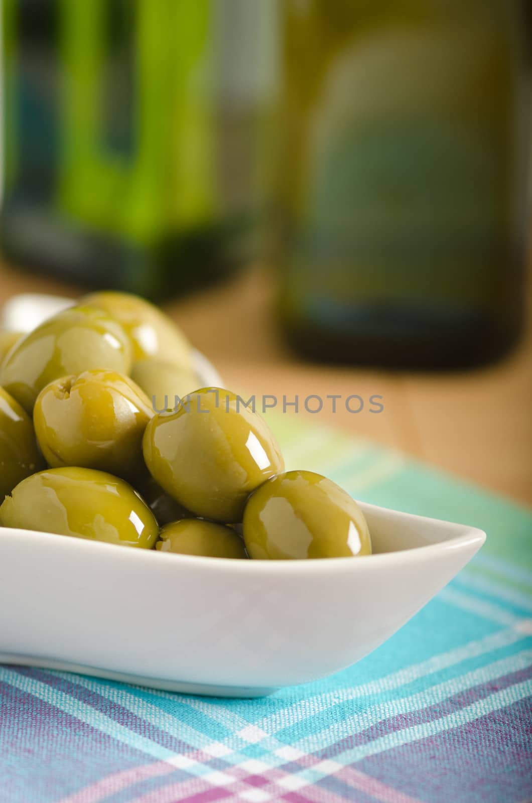Green olives in a bowl and bottles with olive oil on background
