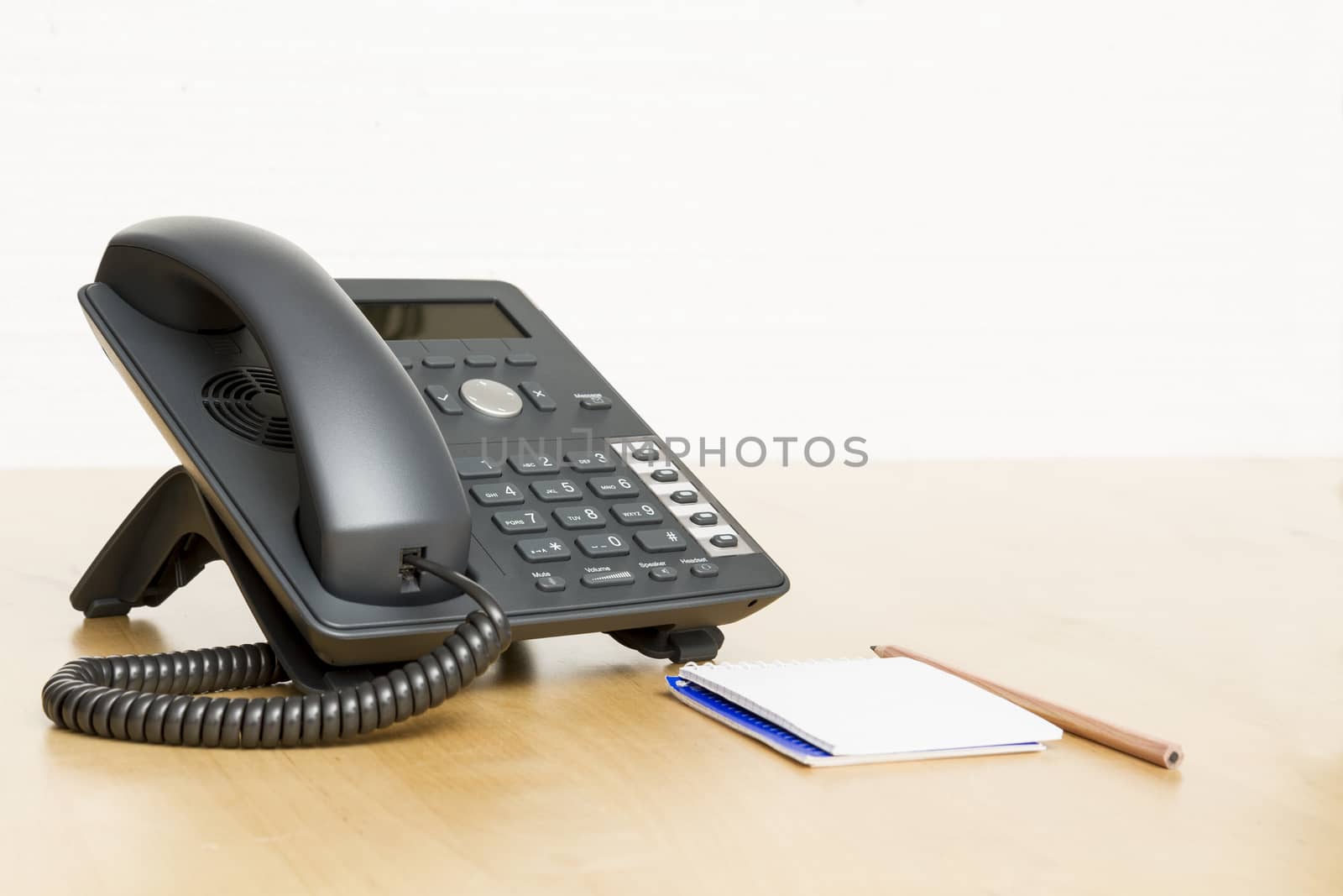 phone on desk with notepad in white background. Wooden desk.
