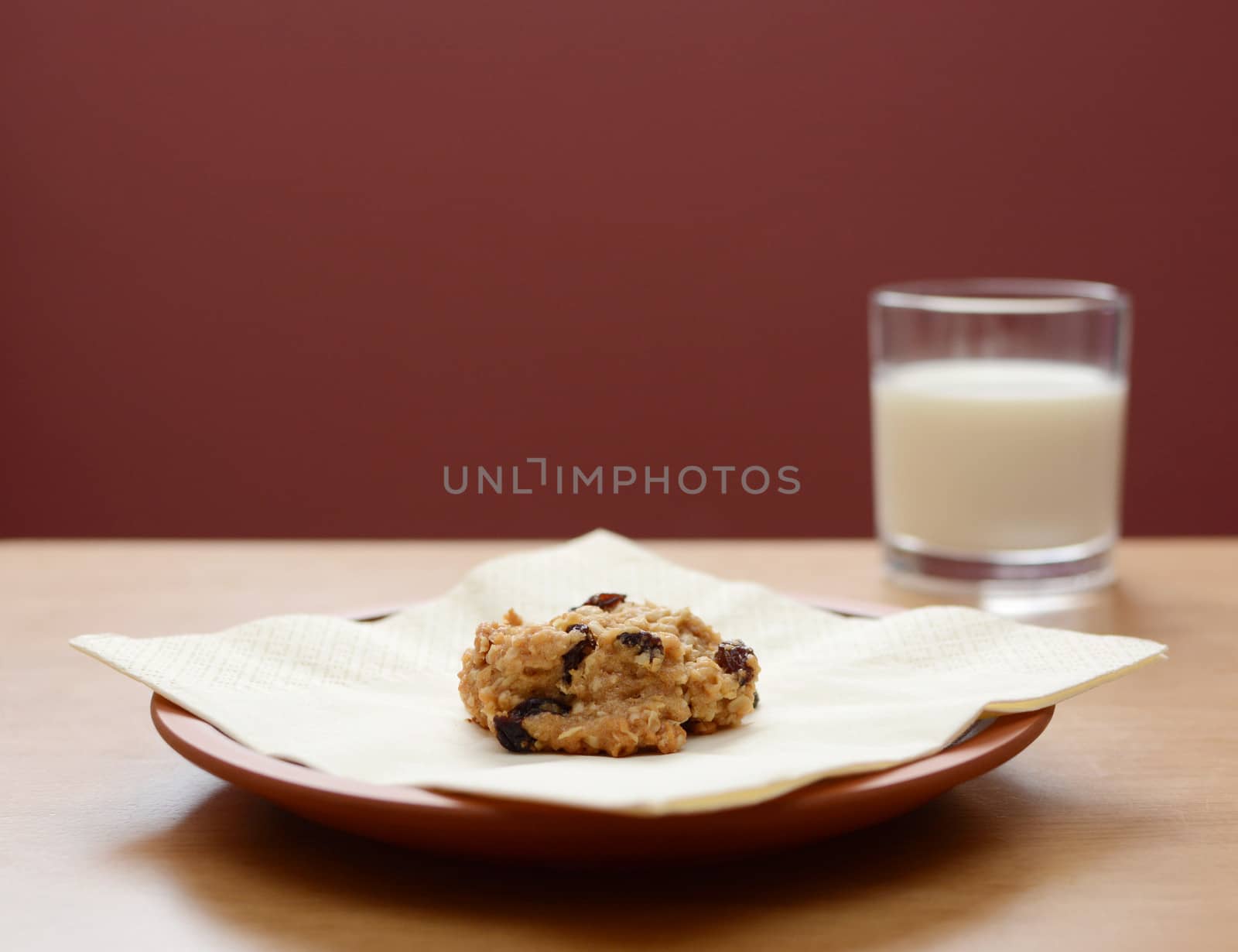 Oatmeal raisin cookie on a plate with a glass of milk in the background