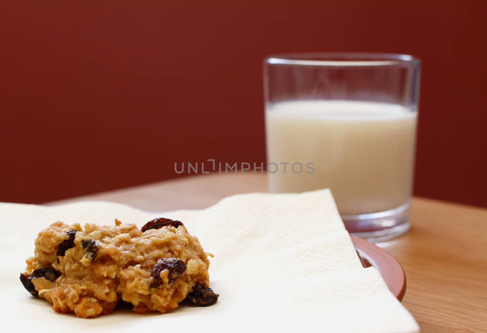 Closeup of a freshly baked oatmeal raisin cookie with a glass of milk