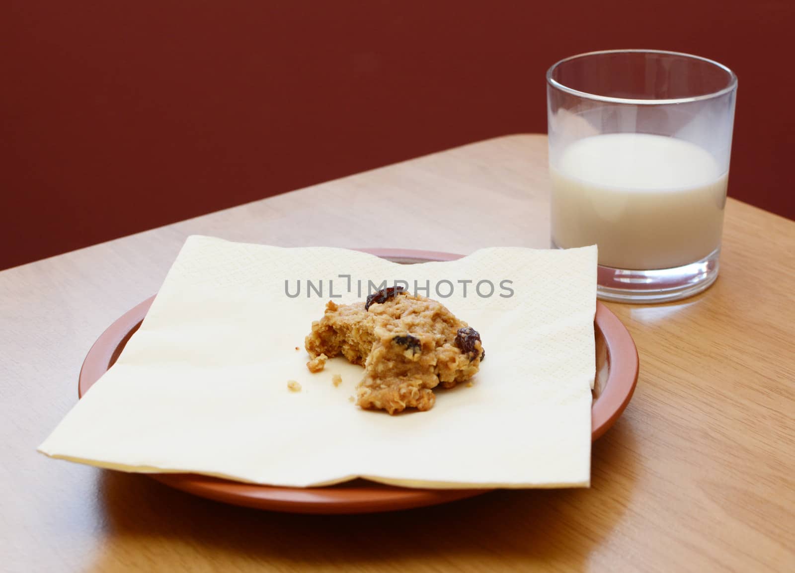 Half-eaten oatmeal raisin cookie with a half drunk glass of milk