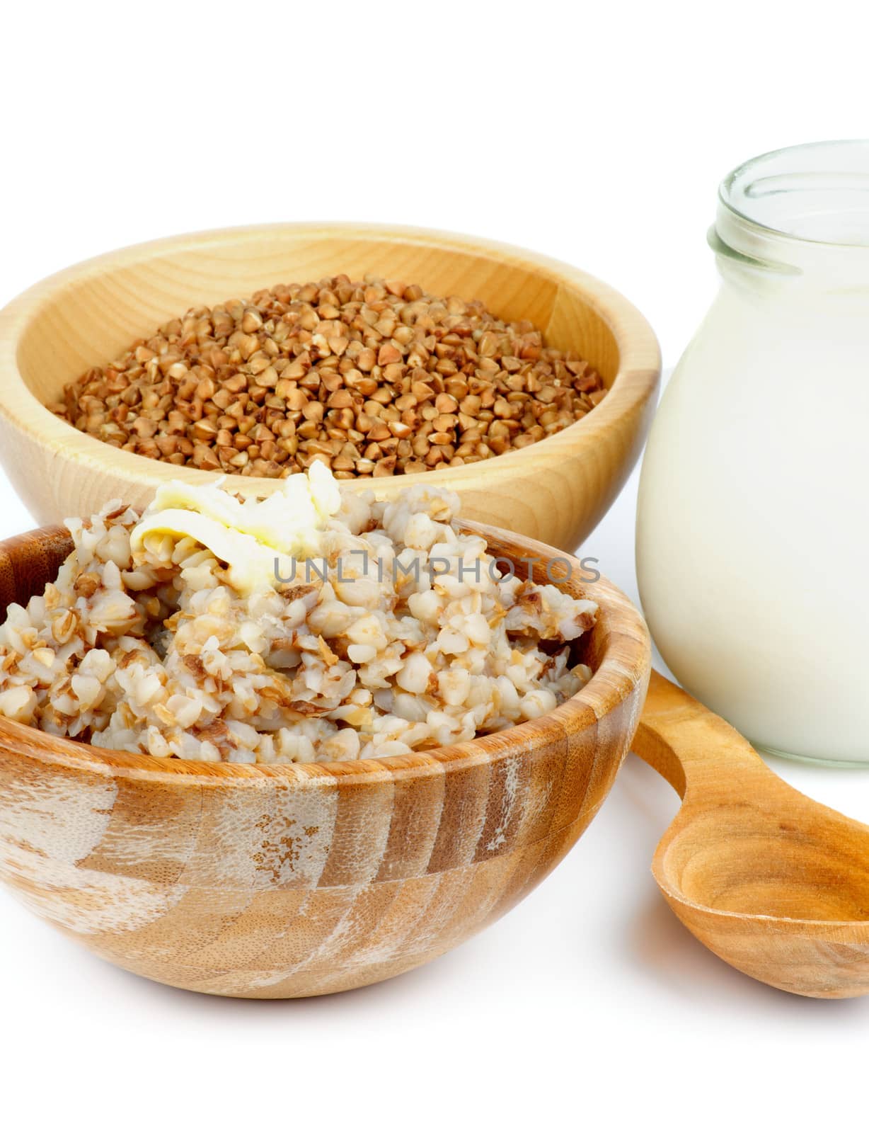 Arrangement of Traditional Russian Buckwheat Kasha with Buckwheat in Wooden Bowl, Milk and Wooden Spoon closeup on white background