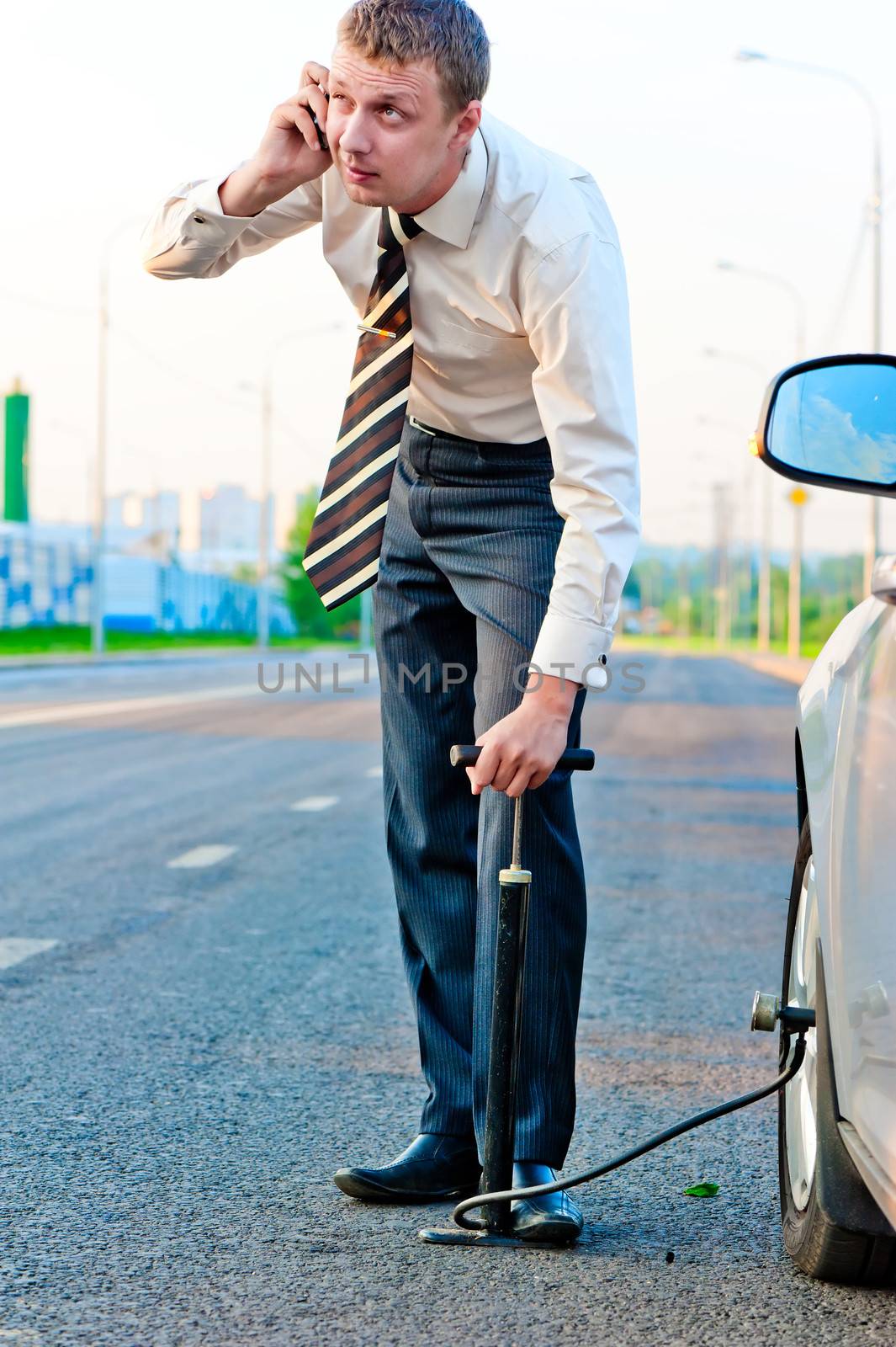 businessman pumps the pump wheel of a car and talking on the phone by kosmsos111