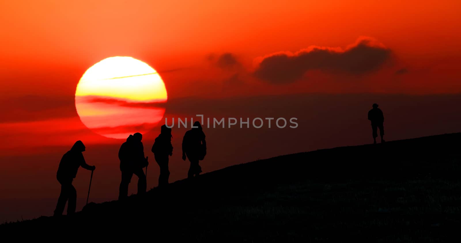 Group of tourists take to the mountains at sunset. Silhouette
