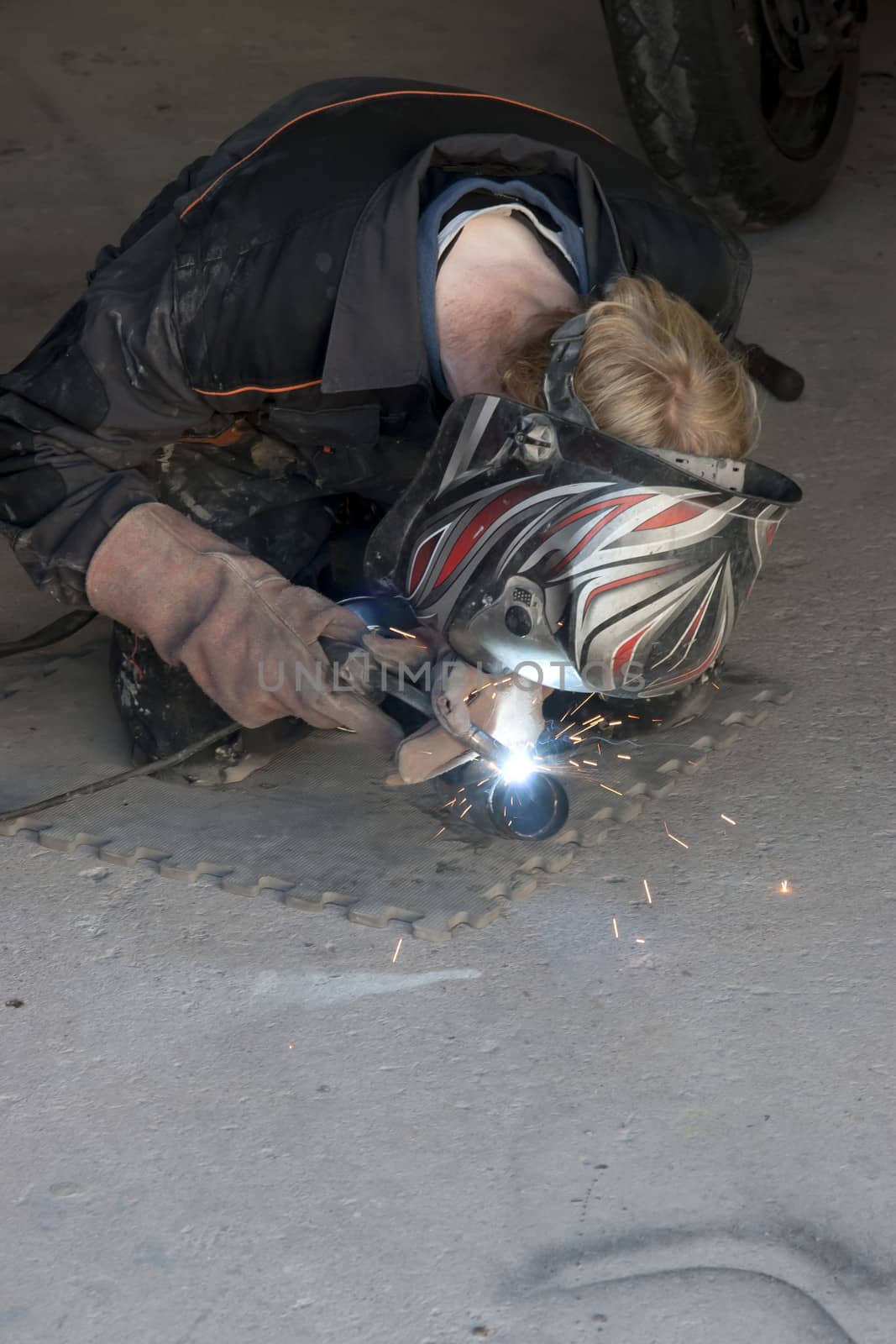 a mechanic welding the exhaust of a motorbike in a garage