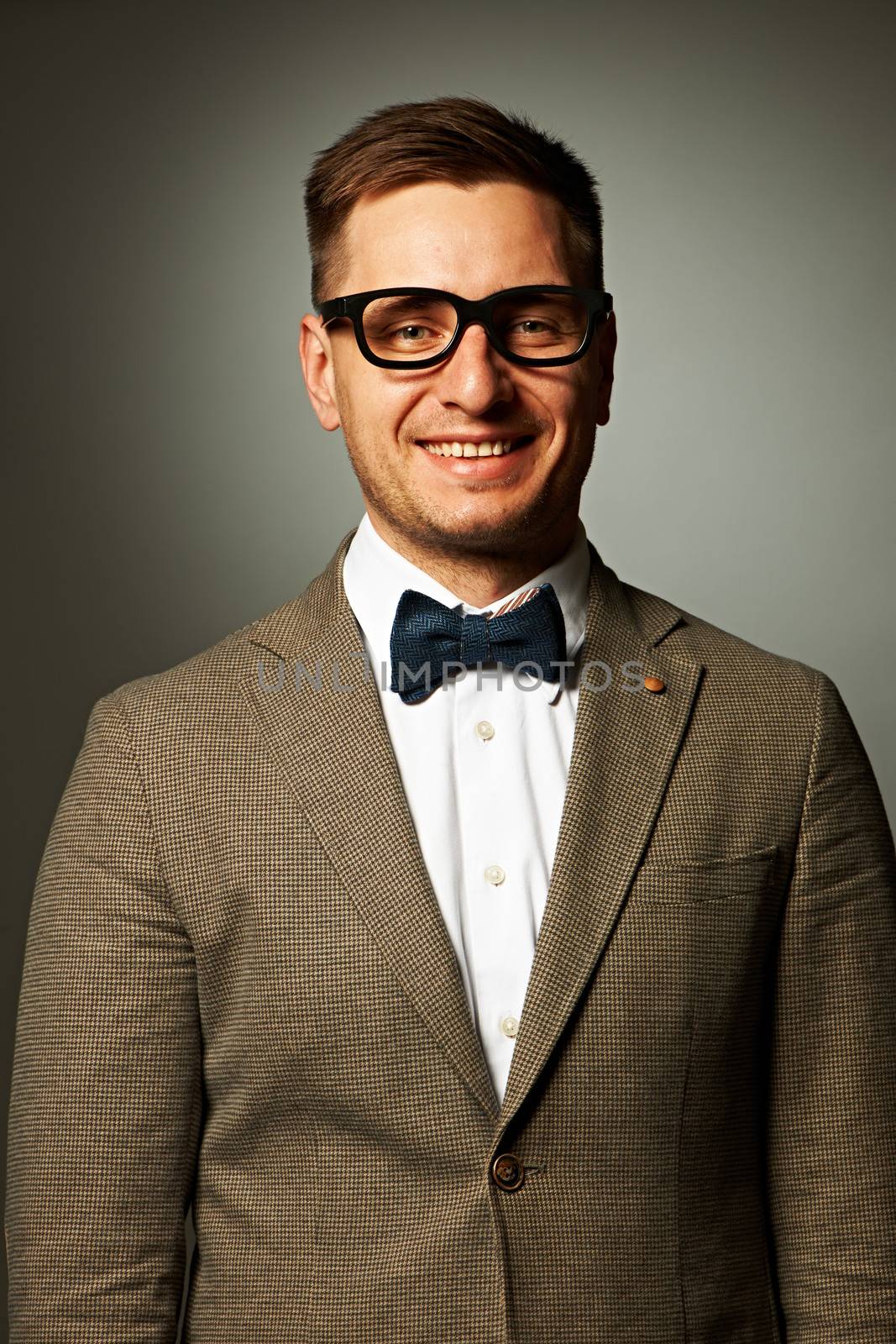 Confident nerd in eyeglasses and bow tie against grey background