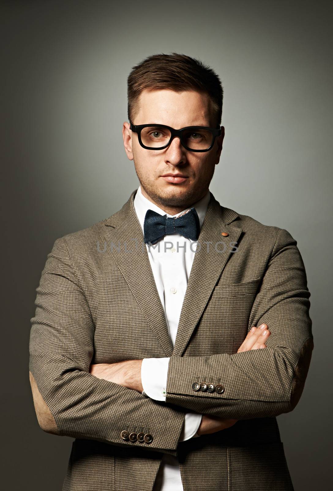 Confident nerd in eyeglasses and bow tie against grey background