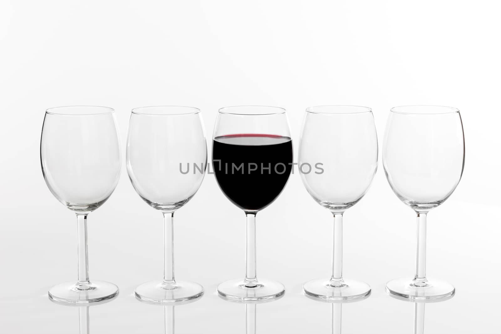 Glass of red wine in a row of empty glasses by anikasalsera