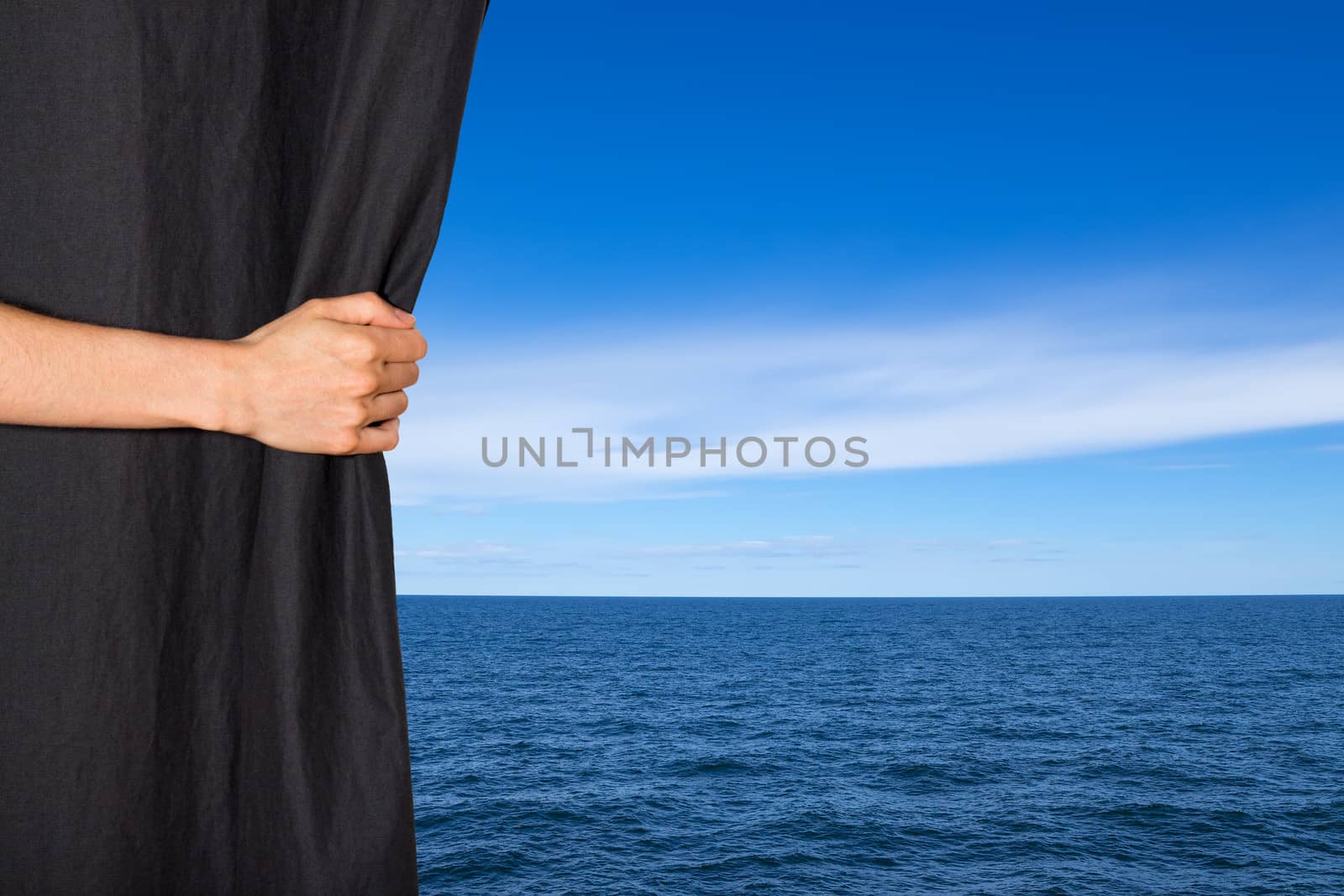 Hand opening black curtain with sea and blue sky behind it.