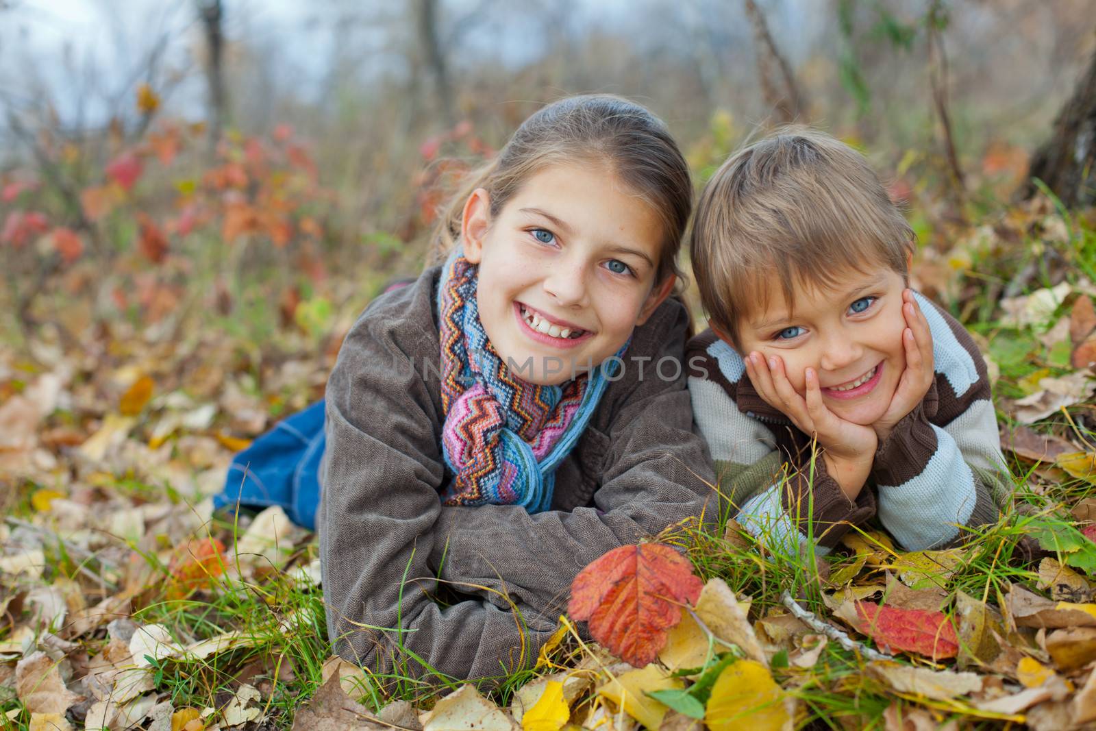 Happy kids lying on autumnal ground covered with dry leaves