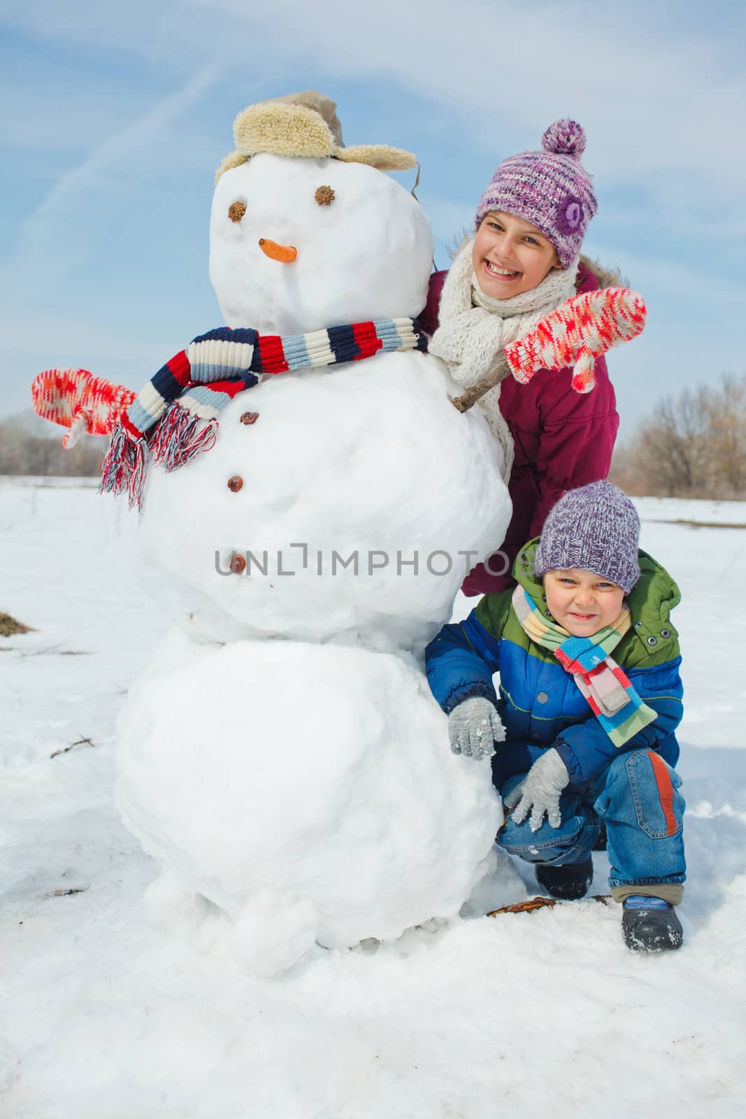 Happy beautiful children with snowman outside in winter time