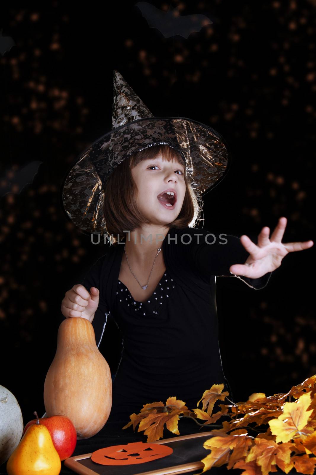 Witch child with pumpkin making magic on halloween, black background