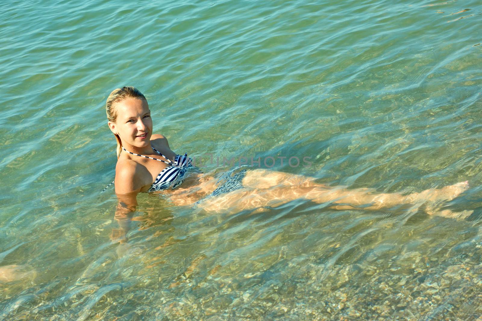 Teen girl on the turquoise sea water surface in shallow coastal area