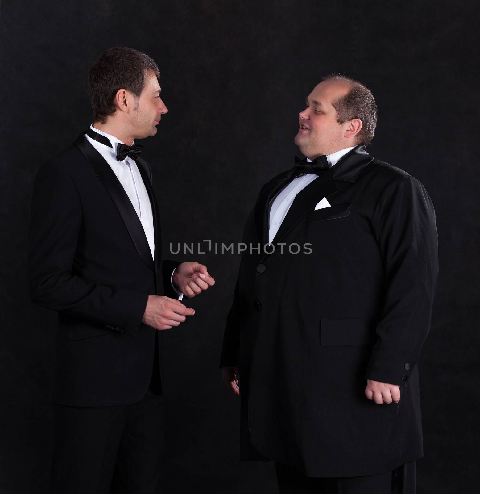 Two stylish businessman in tuxedos, on black background