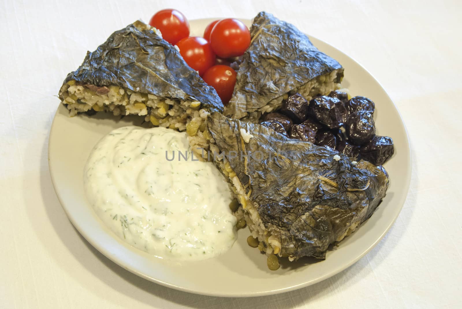 Homemade pie with rice, olives, vegetables, covered with vine leaves, garnished with cherry tomatoes and yogurt with chopped cucumber and garlic