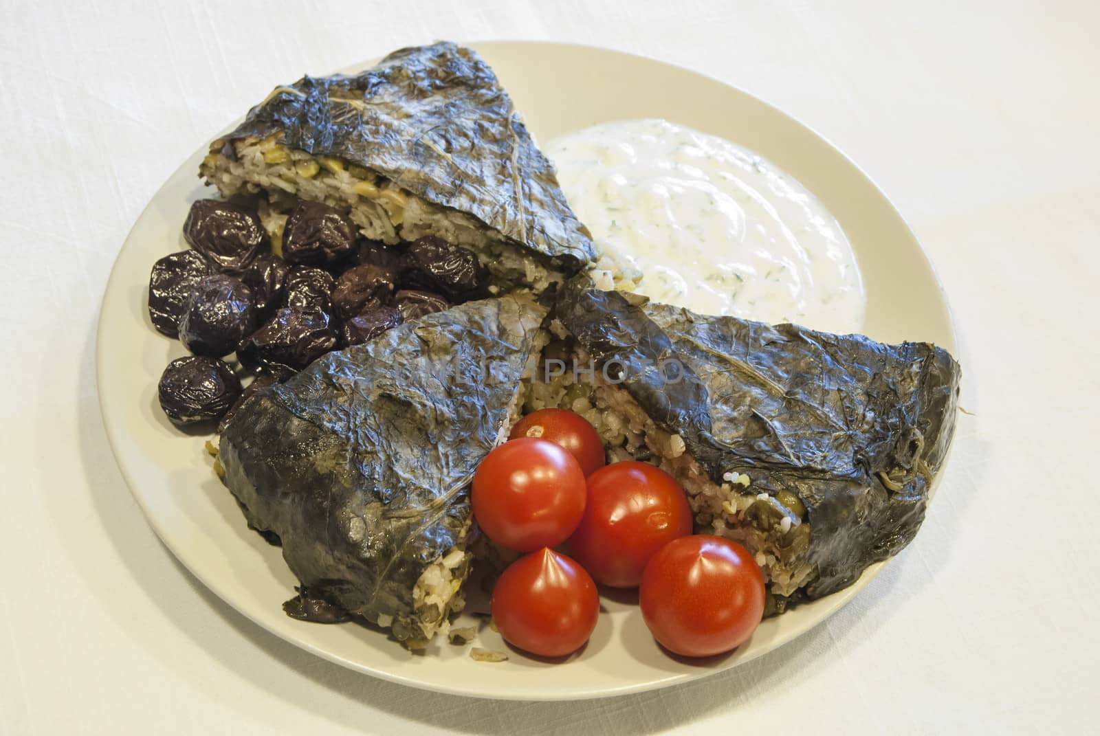 Homemade pie with rice, olives, vegetables, covered with vine leaves, garnished with cherry tomatoes and yogurt with chopped cucumber and garlic