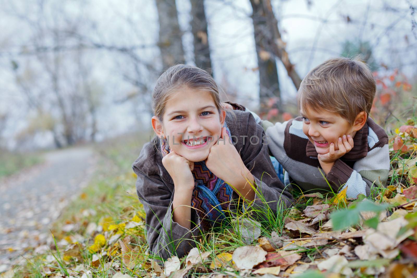 Happy kids lying on autumnal ground covered with dry leaves