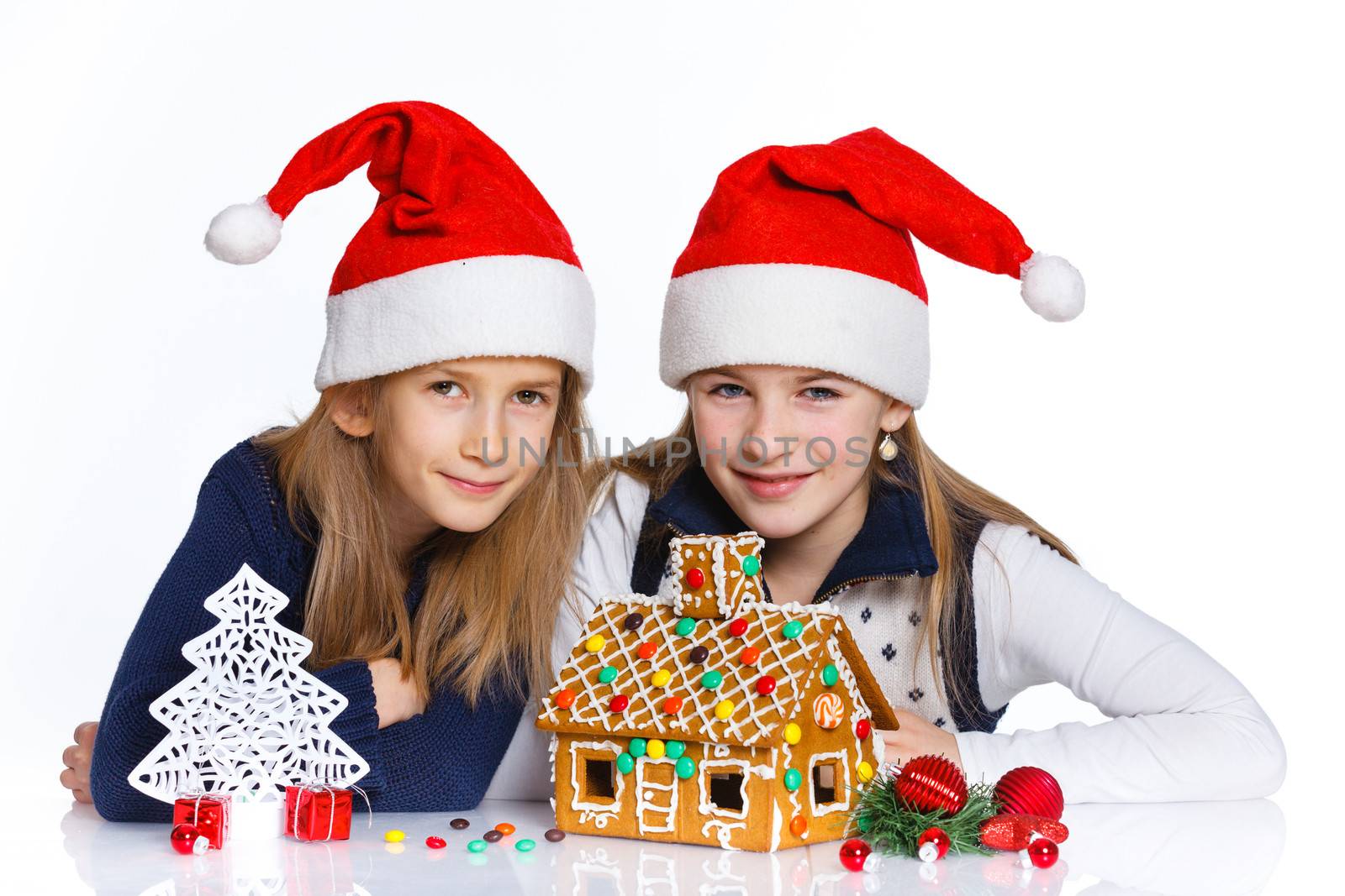 Christmas theme - Two smiling girl in Santa's hat with gingerbread house, isolated on white