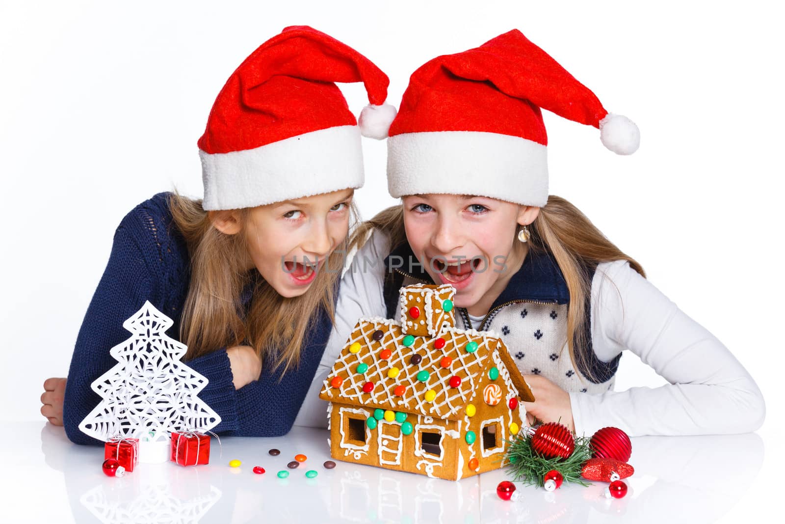 Christmas theme - Two smiling girl in Santa's hat with gingerbread house, isolated on white