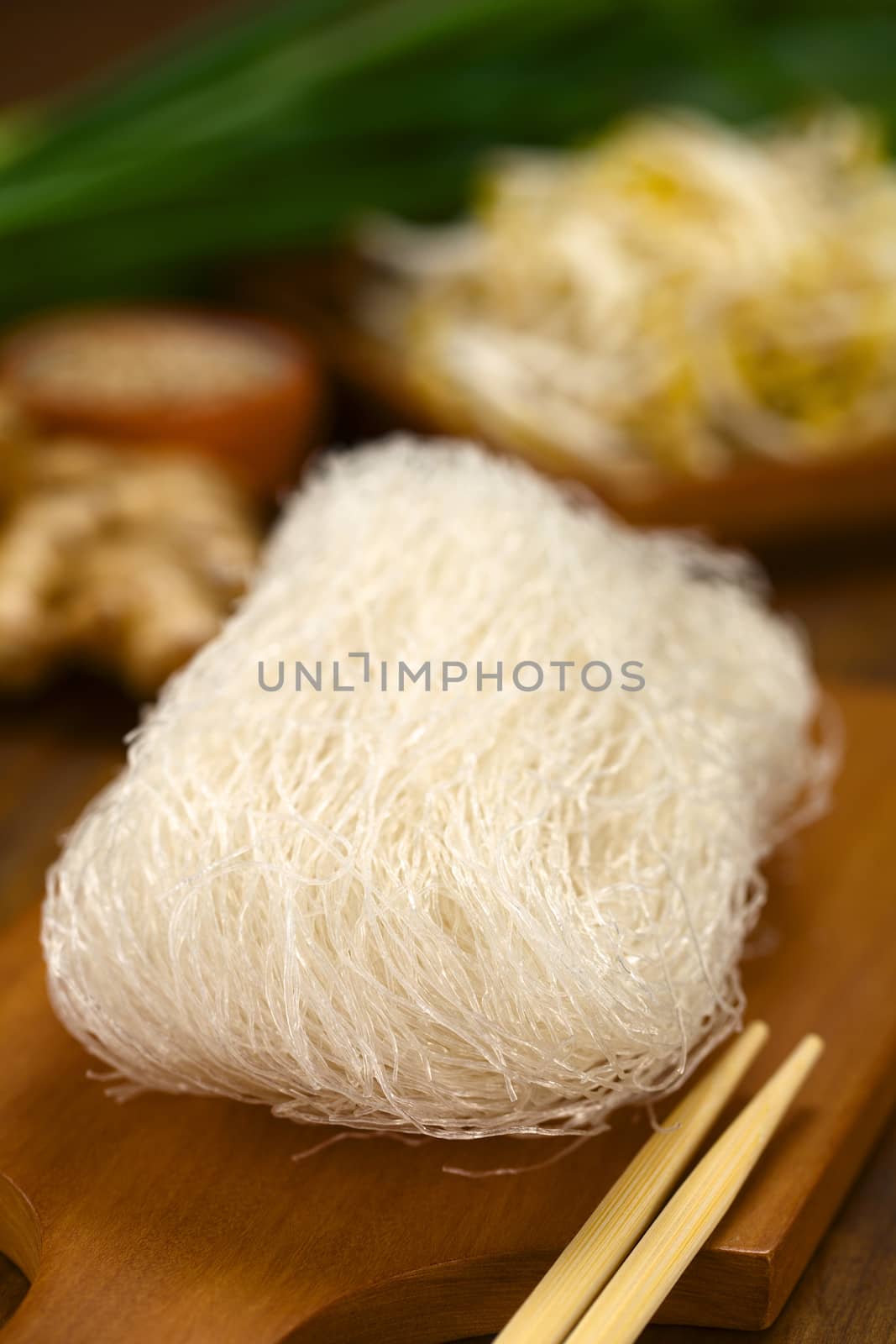 Raw rice noodles on wooden board with chopsticks on the side and vegetables in the back (Selective Focus, Focus on the right front part of the noodles)