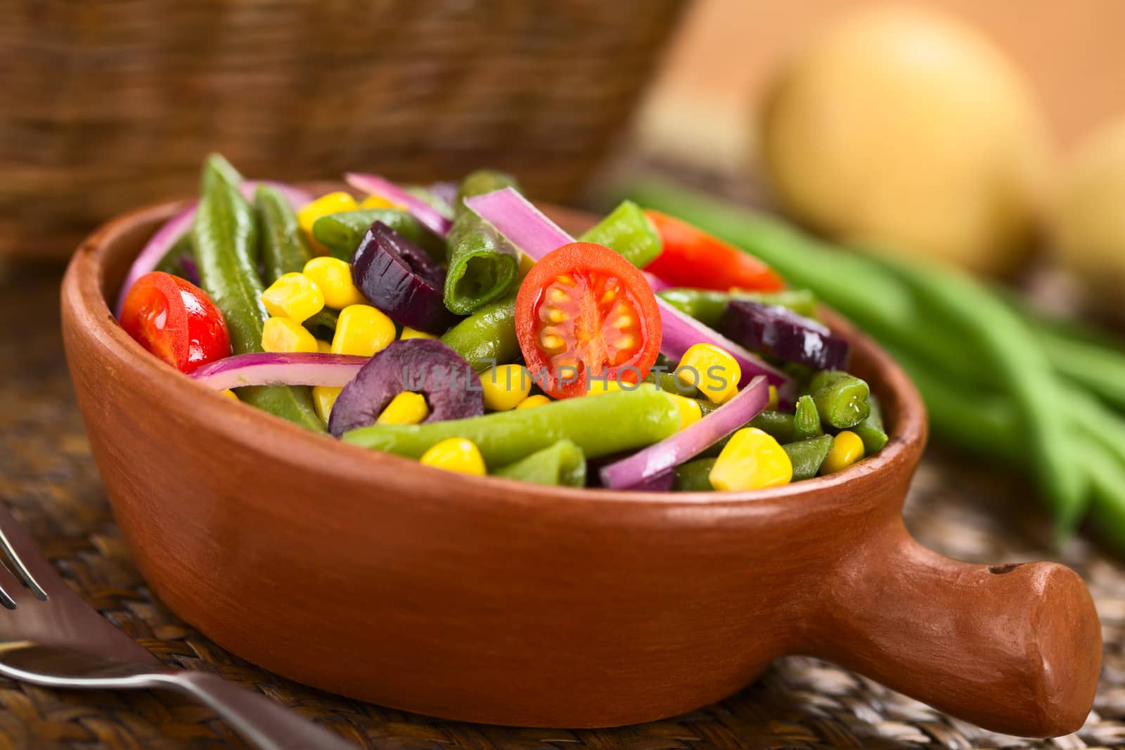Fresh colorful vegetarian salad made of green beans, cherry tomatoes, sweet corn, black olives and red onions in rustic bowl (Selective Focus, Focus on the tomato in the middle) 