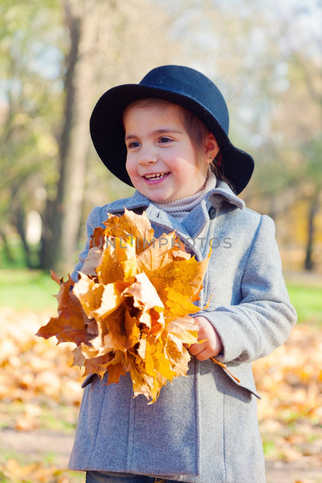 child the girl in a coat and a hat to stand with a bouquet of maple leaves